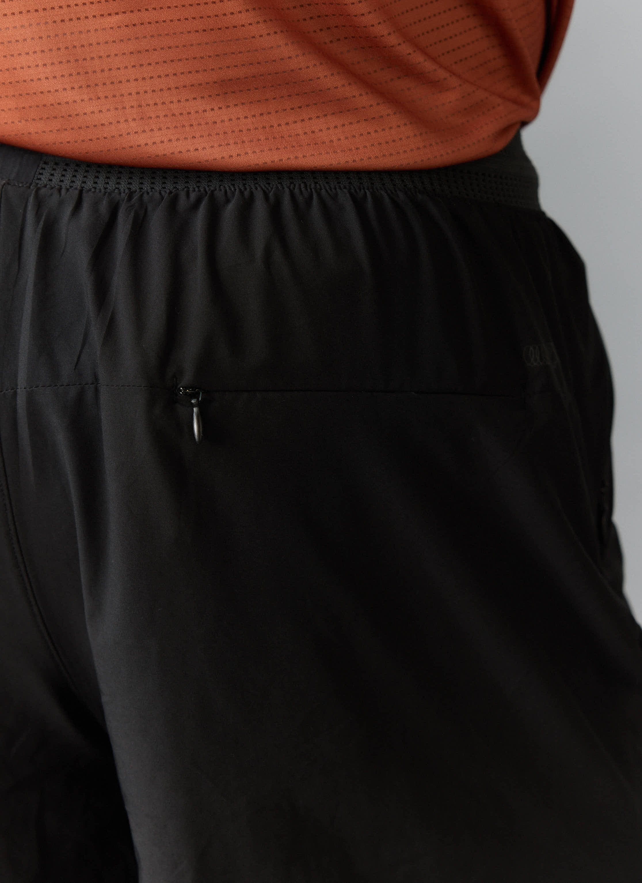 A close-up of the black PCVL 2 in 1 Shorts by Percival, highlighting the secure rear zip pocket and waistband detail.