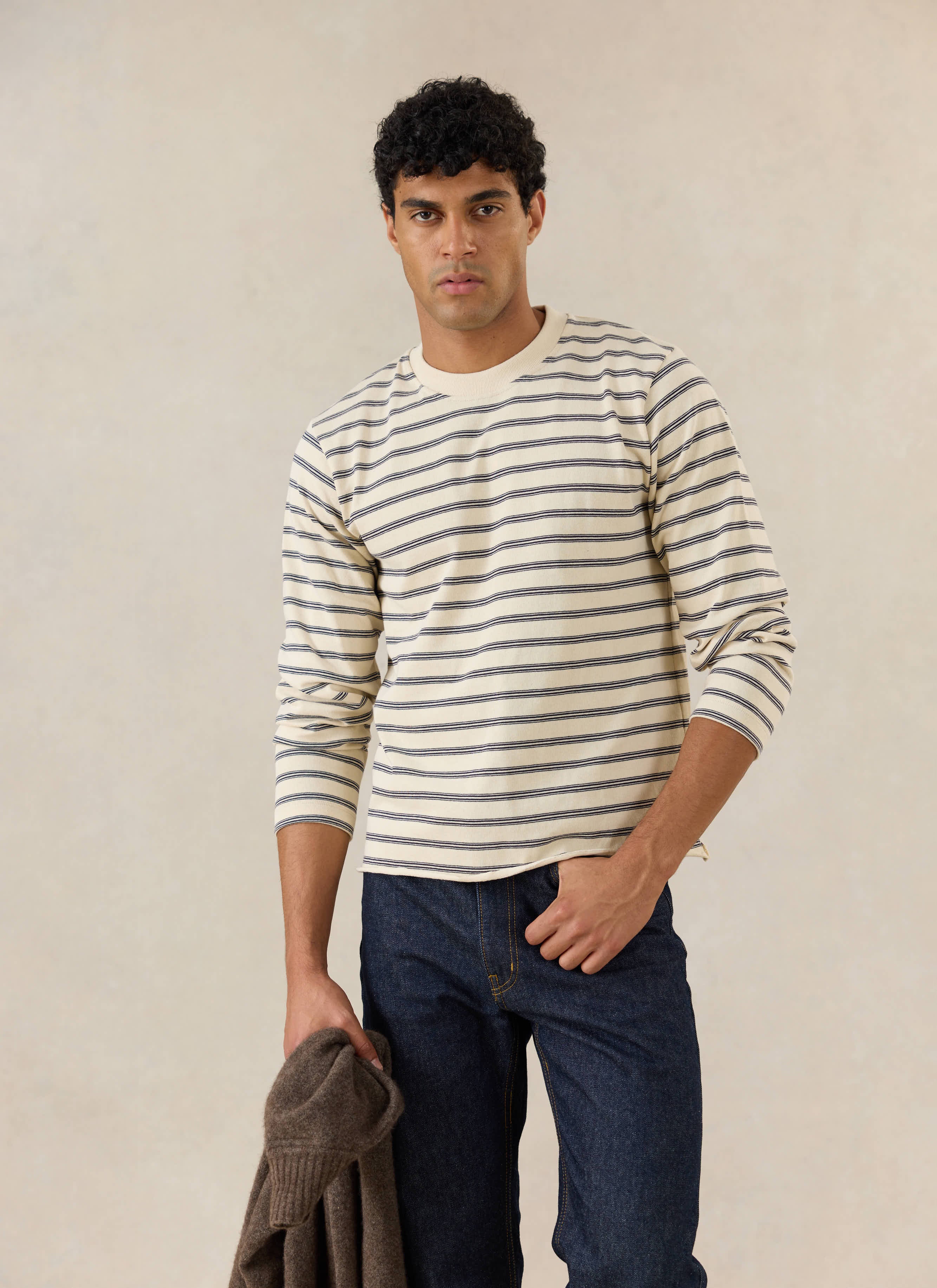 A model wears the white stripe Percival Arlo Raw Hem Long Sleeve Breton T-shirt, styled with dark jeans.