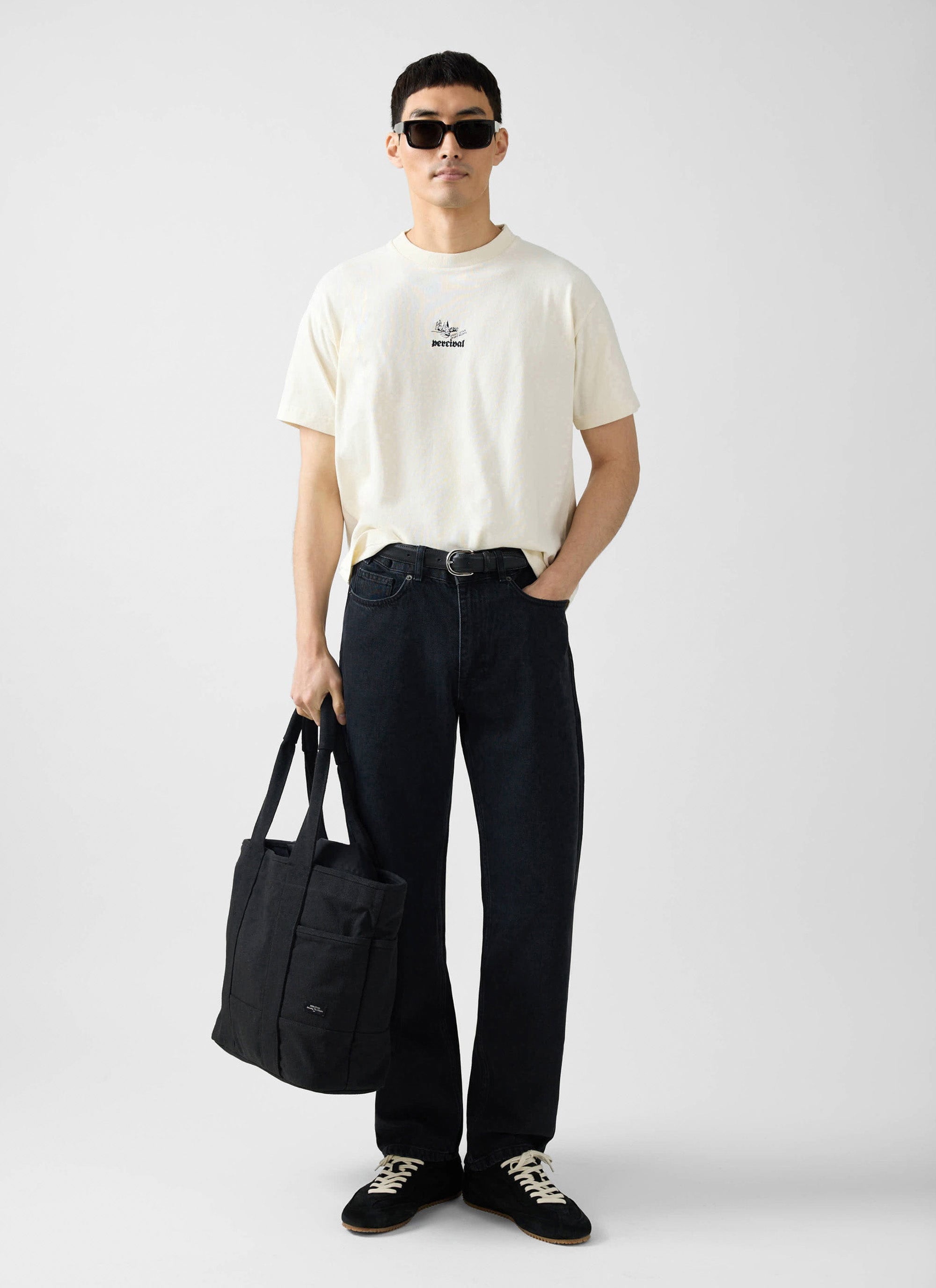 A model wears the Percival Wildlands oversized t-shirt in ecru, styled with black jeans, sunglasses, and a tote bag.