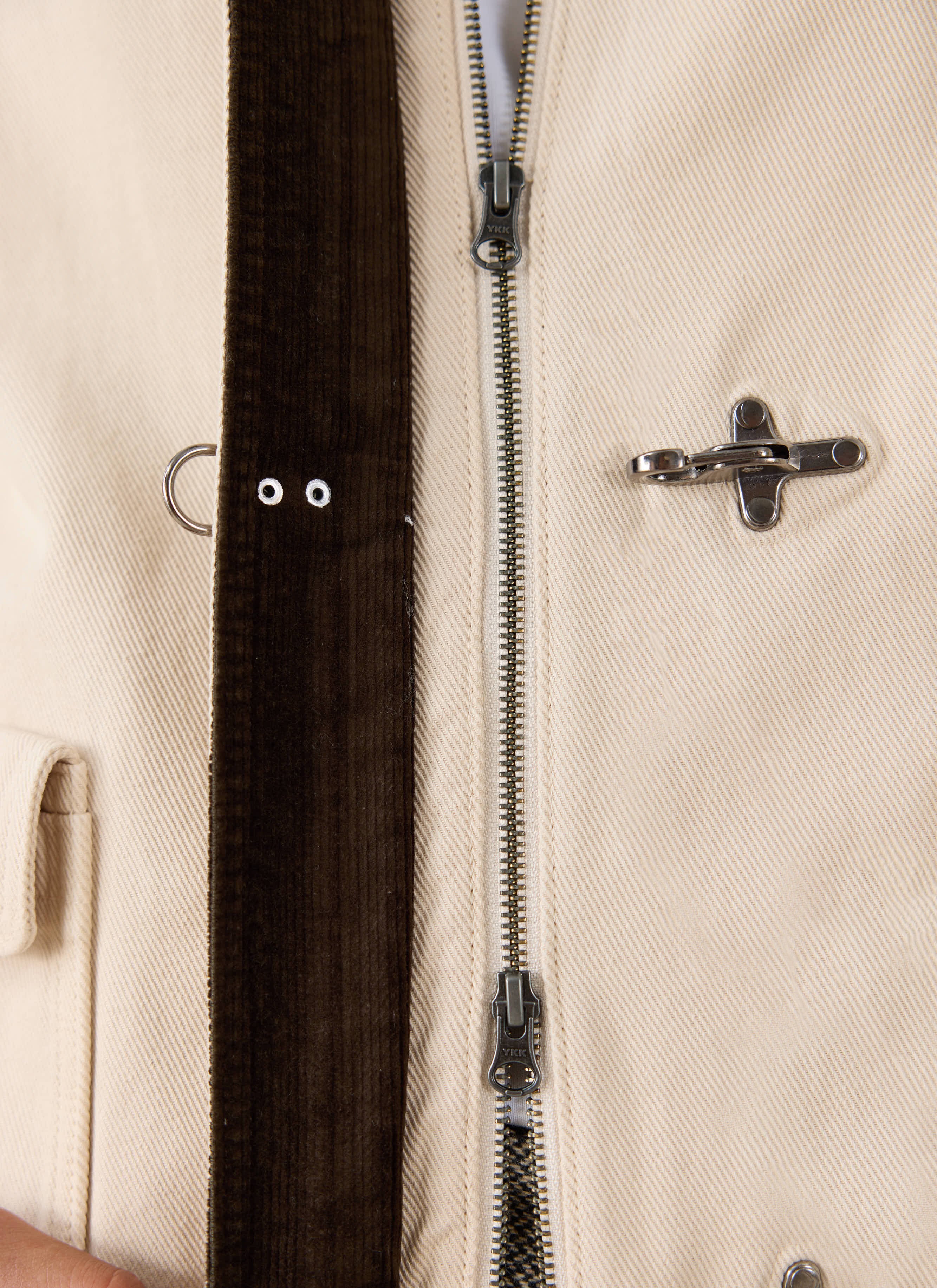 Close-up of the cream cotton Percival jacket, highlighting the dark brown corduroy placket, metal zipper, and fireman clasp.
