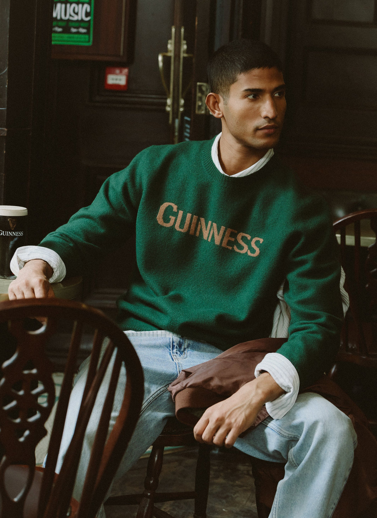 Model wearing the Guinness x Percival forest green merino wool jacquard jumper while sitting inside a pub.