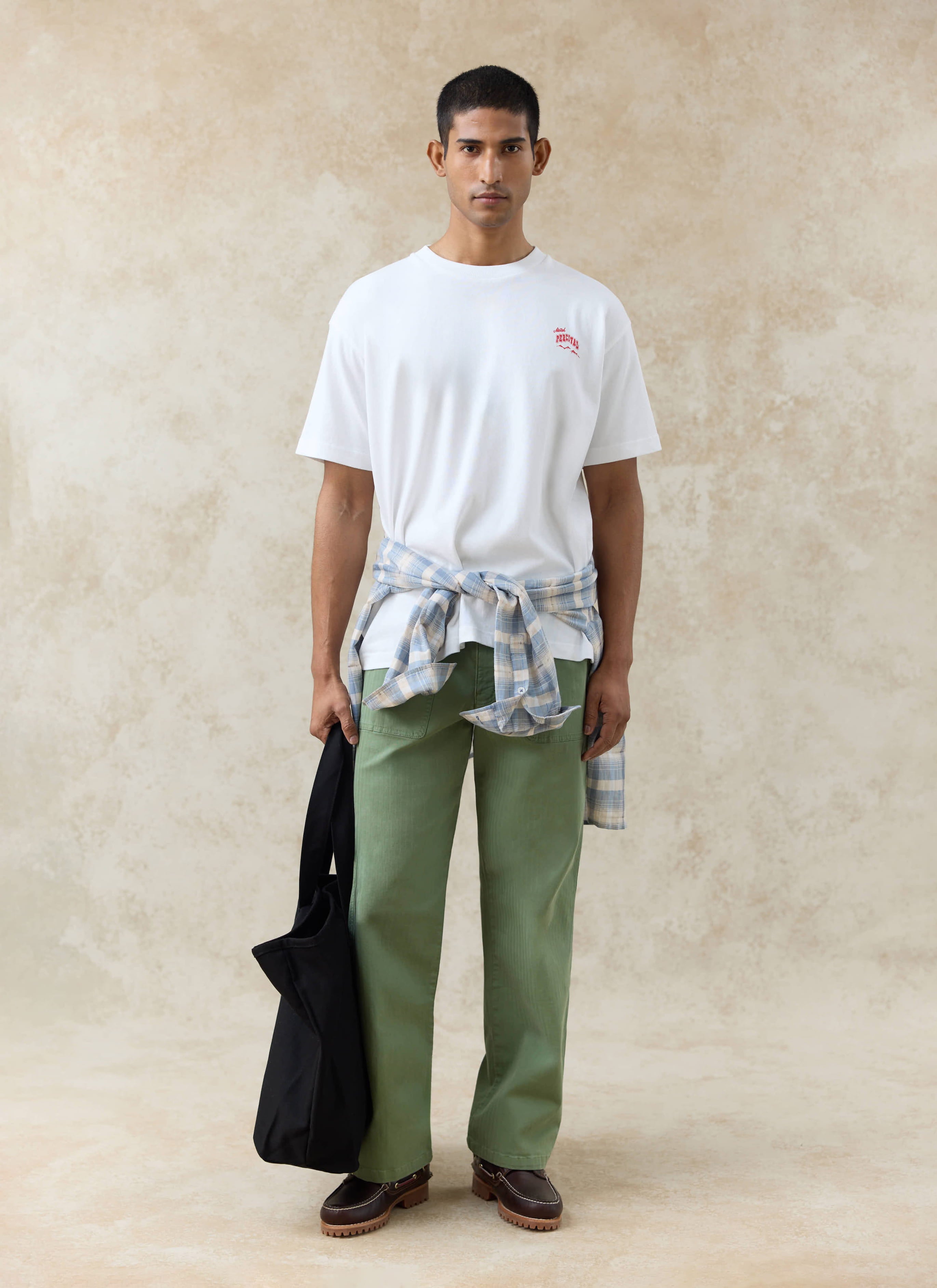 White Percival Gordon Oversized T Shirt in organic cotton, paired with green trousers and a checked shirt at the waist.