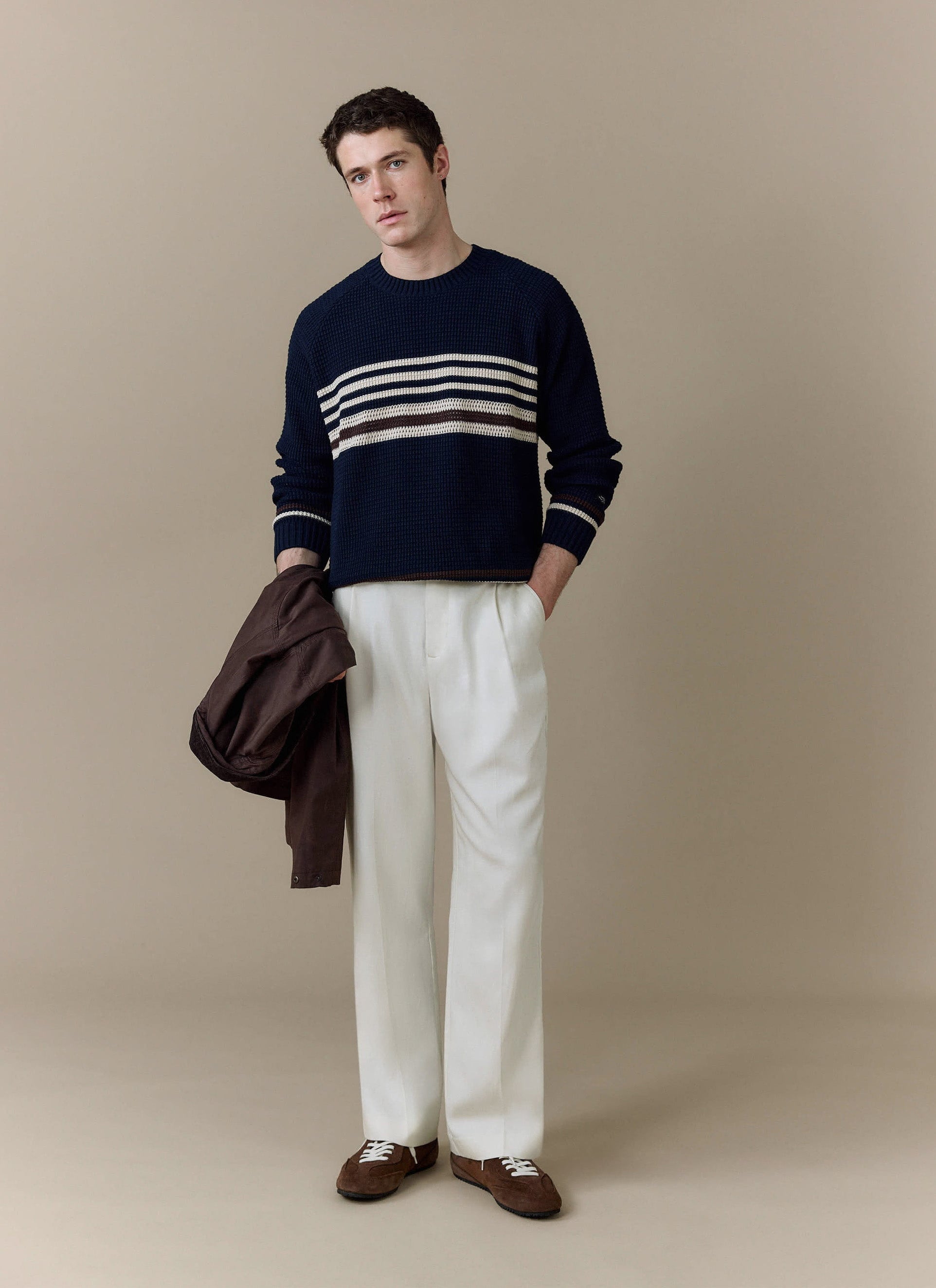 A model wears the Percival Sergio Crochet Jumper in navy, a striped cotton knit, styled with white trousers and a jacket.