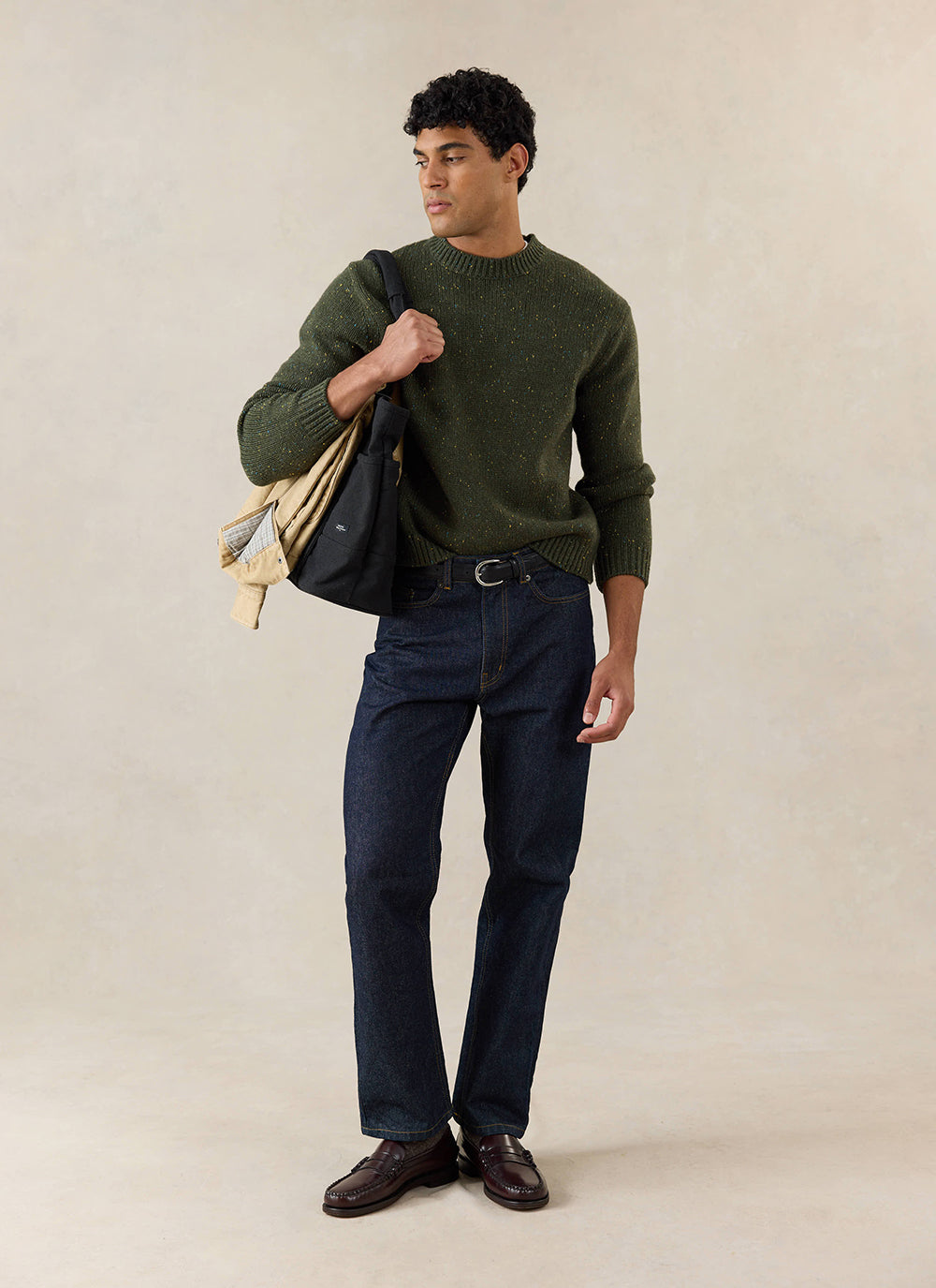 A model wears the forest green Percival Rhodes crew neck jumper, styled with dark jeans and a black shoulder bag.