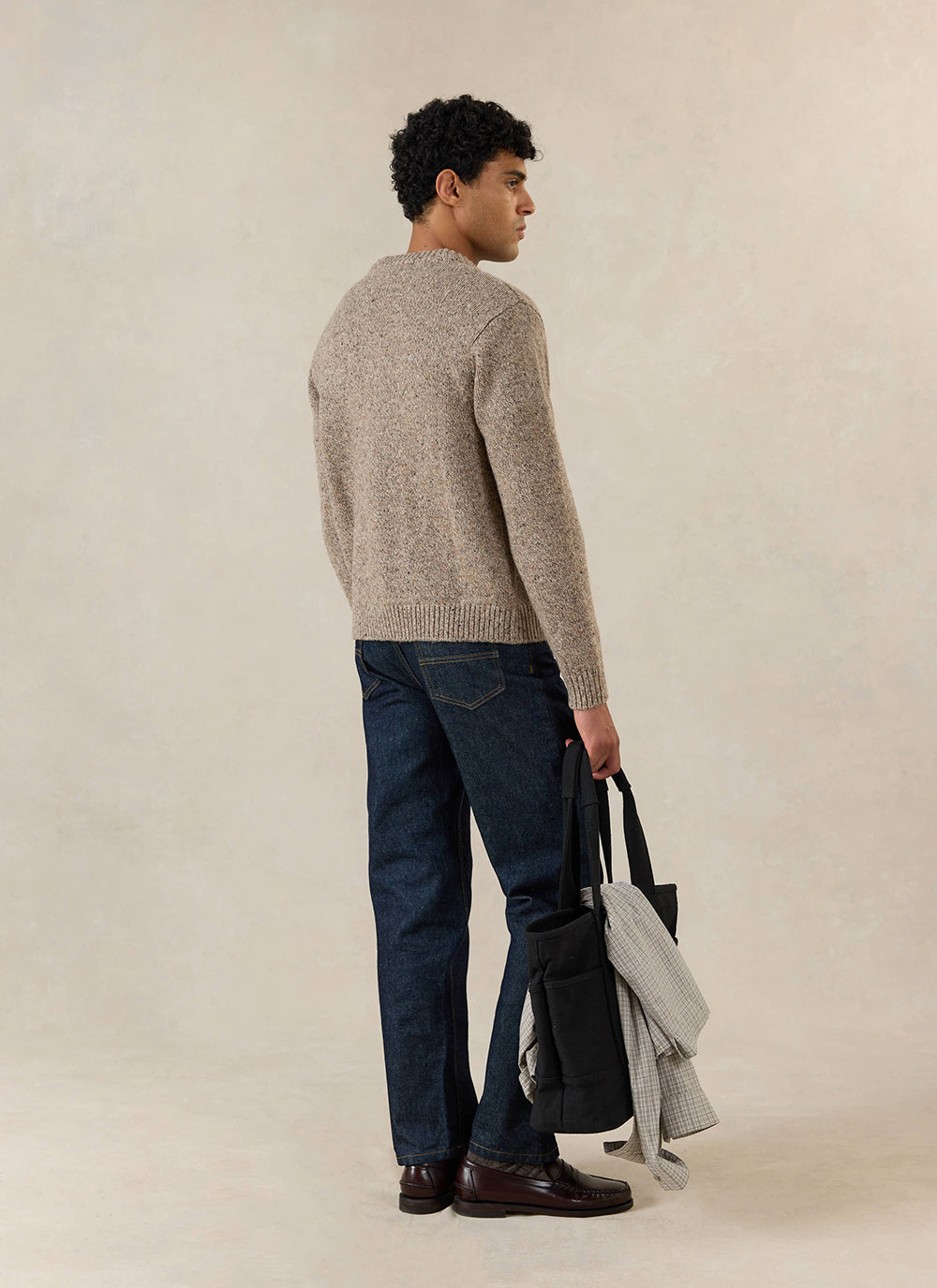 A model wears the Percival Rhodes Cardigan in oak cotton, styled with dark jeans, loafers and a black bag, seen from behind.