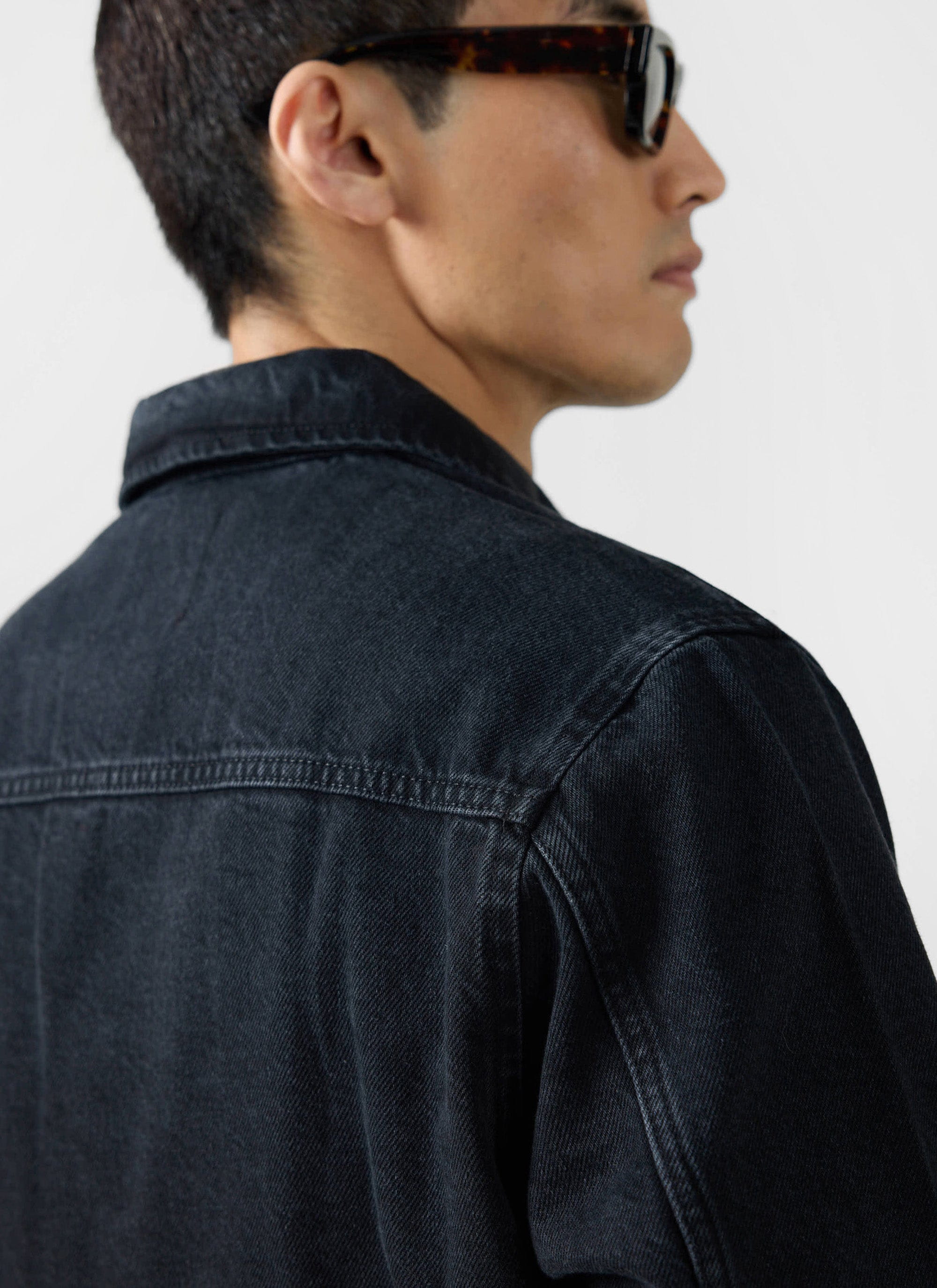 Close-up of a model wearing the Percival Gove Chore Jacket in black denim, showing the shoulder and collar detail.