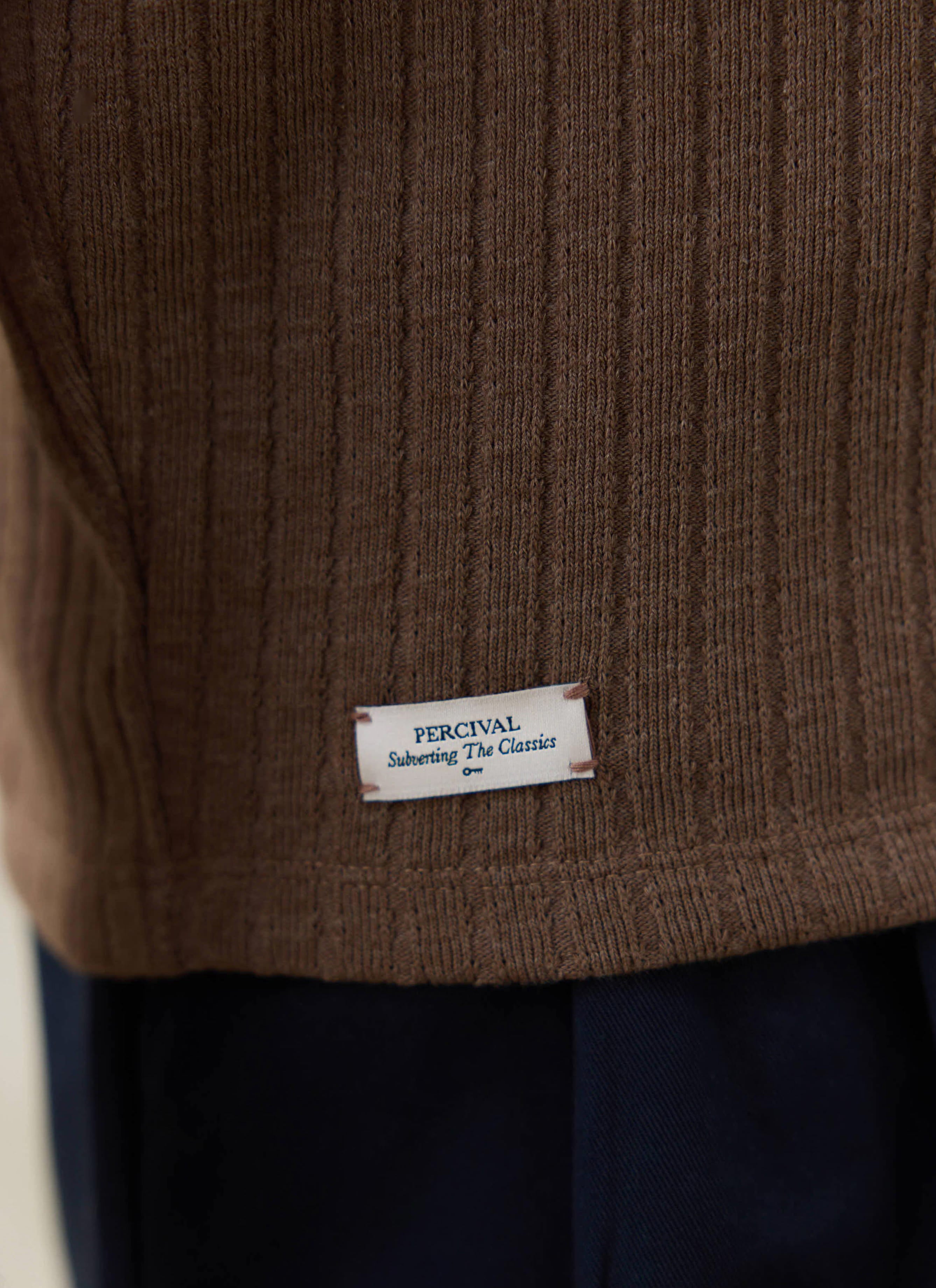Close-up of the espresso brown ribbed knit fabric on the Percival Anthony Polo, featuring the white brand hem tag.