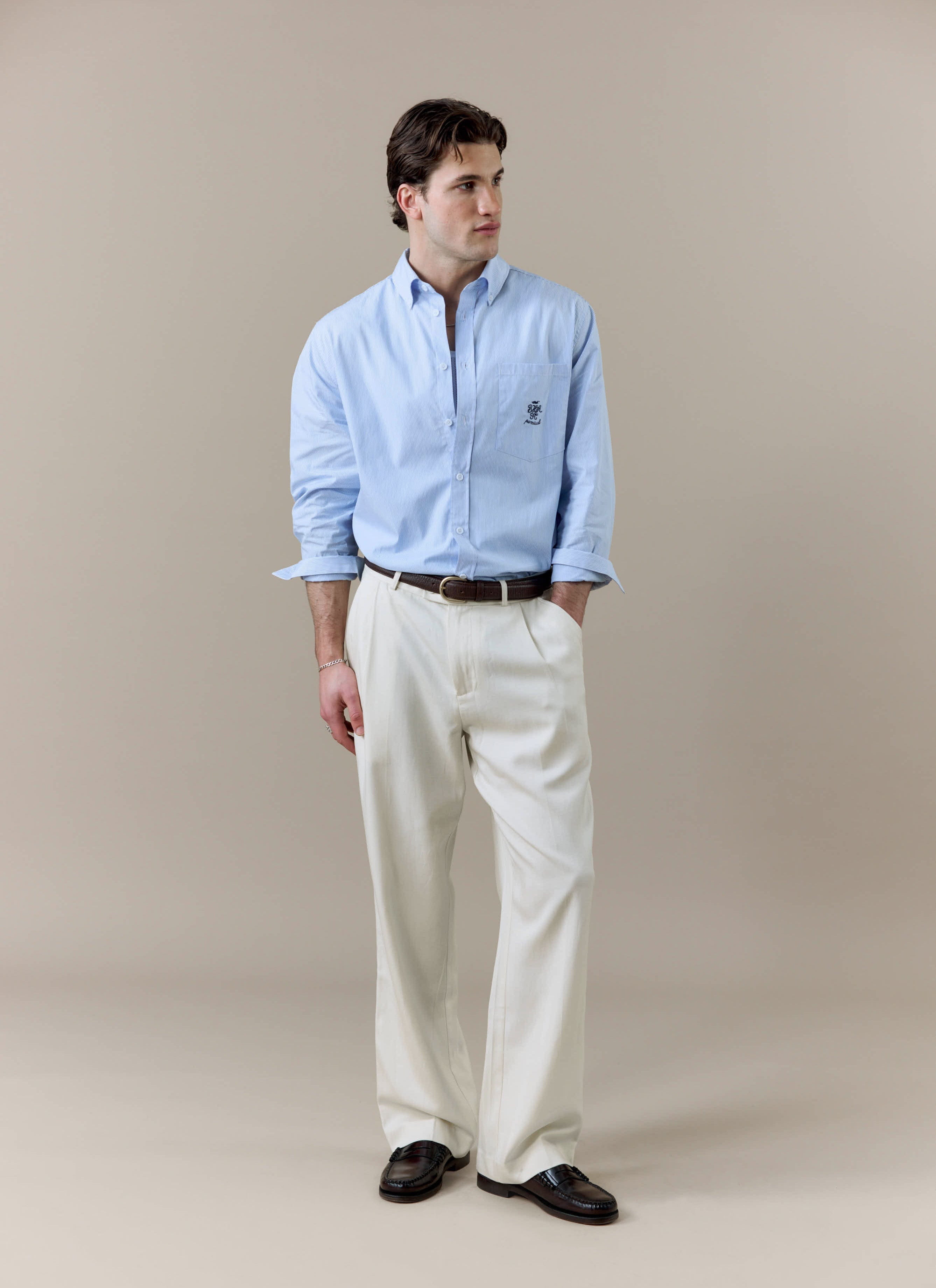 A model wears the blue and white striped Pearce Long Sleeve Shirt from Percival, styled with white trousers and loafers.