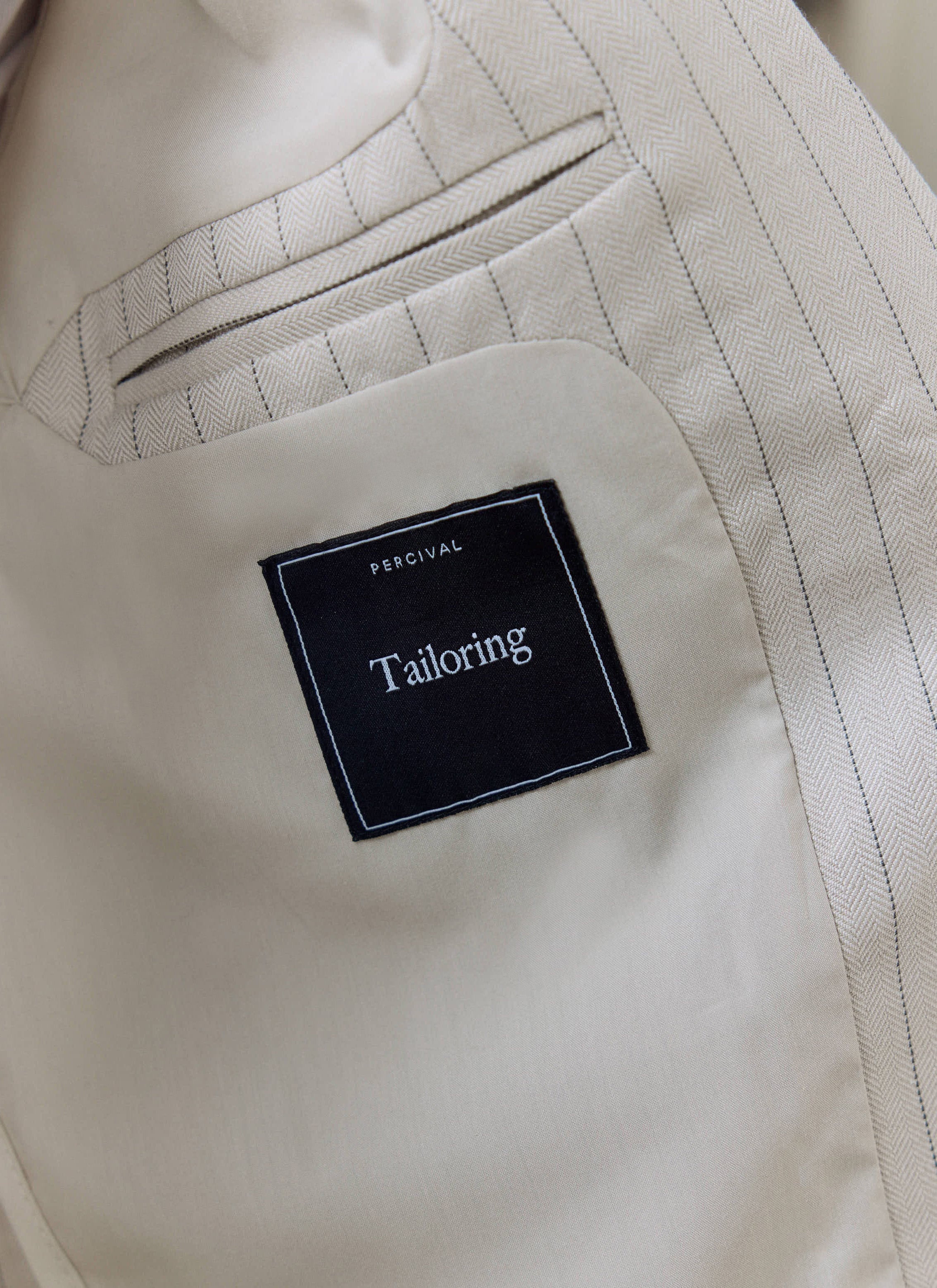 A close-up detail shot of the interior label and lining on a Percival cream striped tailored blazer.