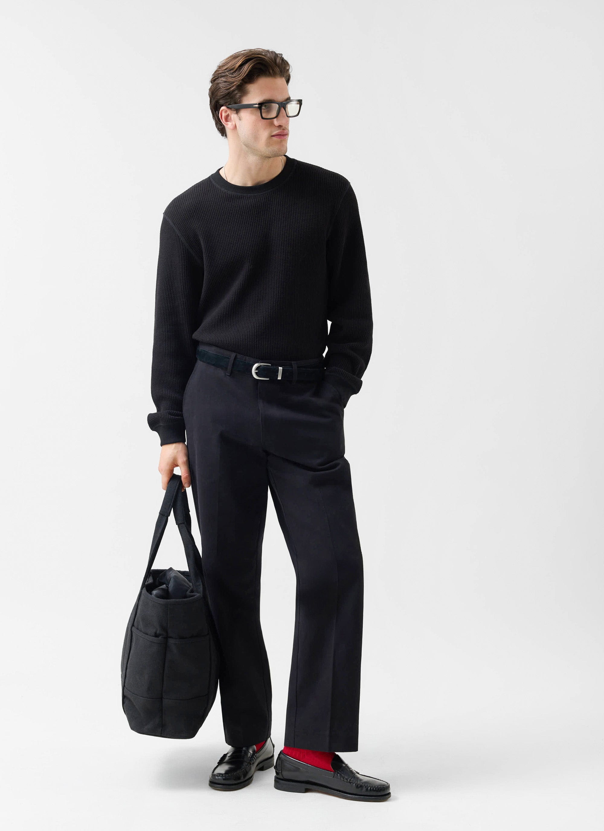 A model wears the Percival Straight Leg Chino in black, paired with a matching jumper, loafers and a tote bag.