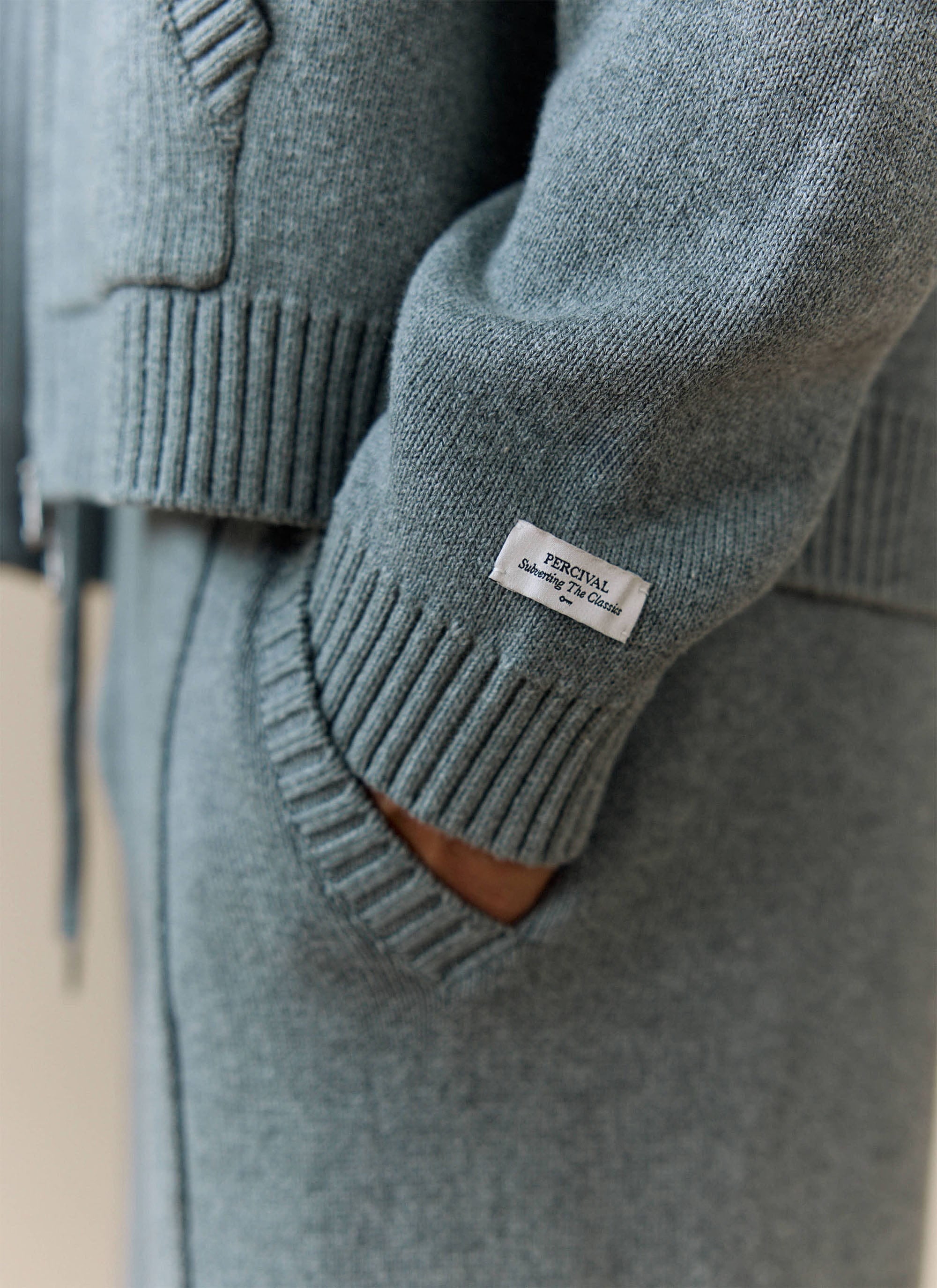Close-up of the Percival brand label on the ribbed cuff of the grey Chronicle Knitted Hoodie, showing the fine cotton knit.