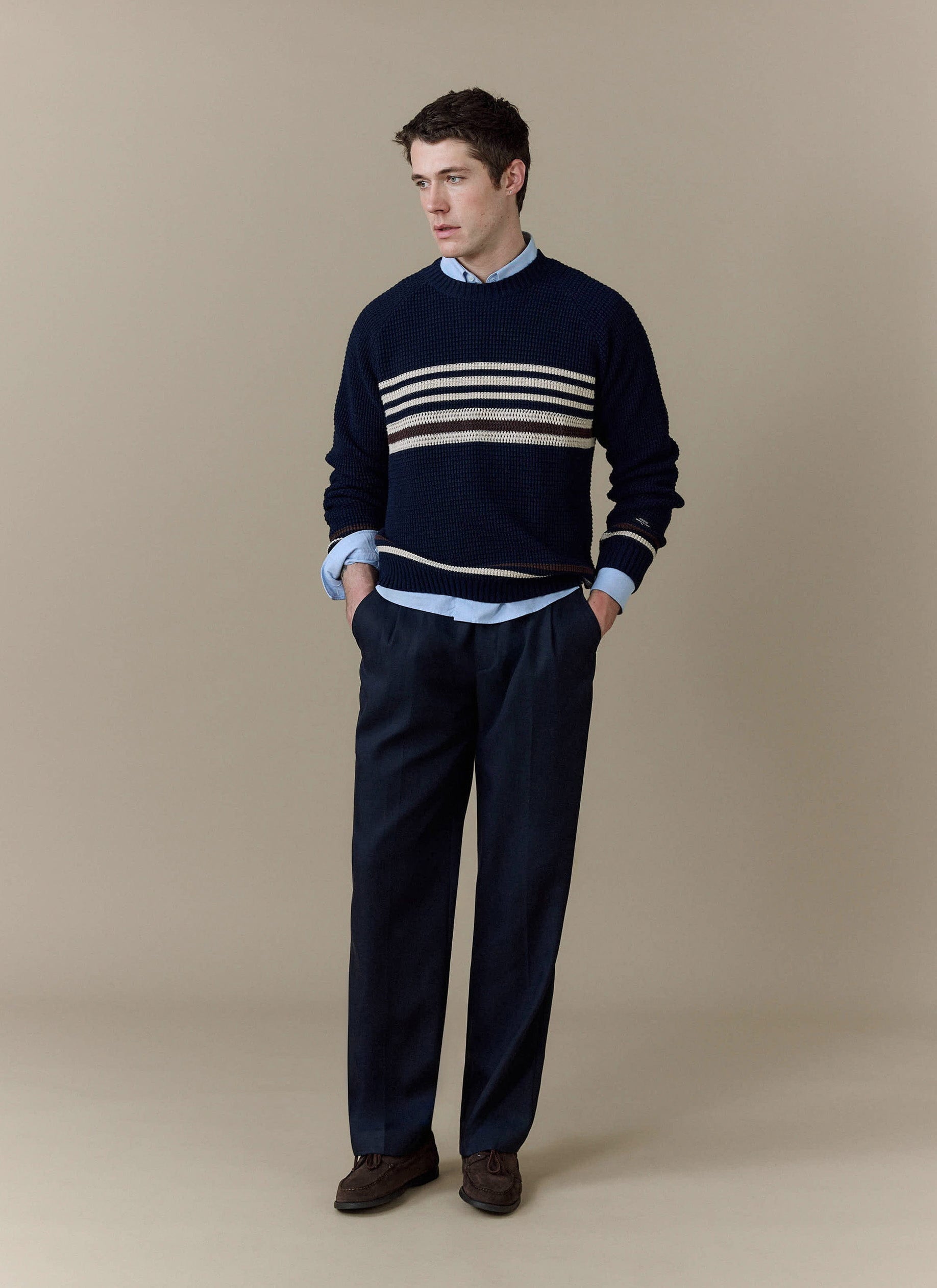 A man models the navy Sergio Crochet Jumper from Percival, styled over a light blue shirt with smart navy trousers.