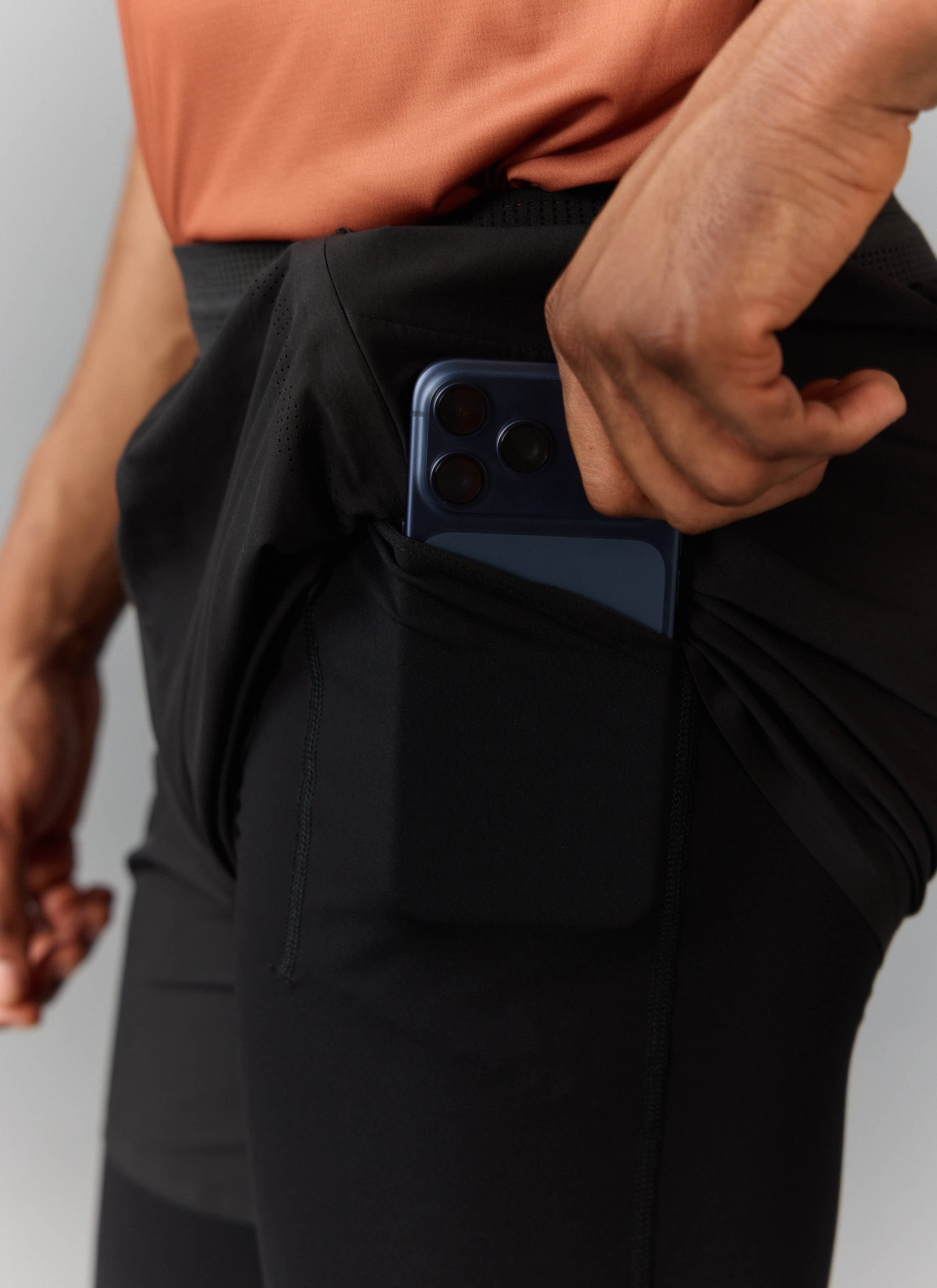Close-up of a phone being placed into the secure rear pocket of the black PCVL 2 in 1 Shorts from Percival.