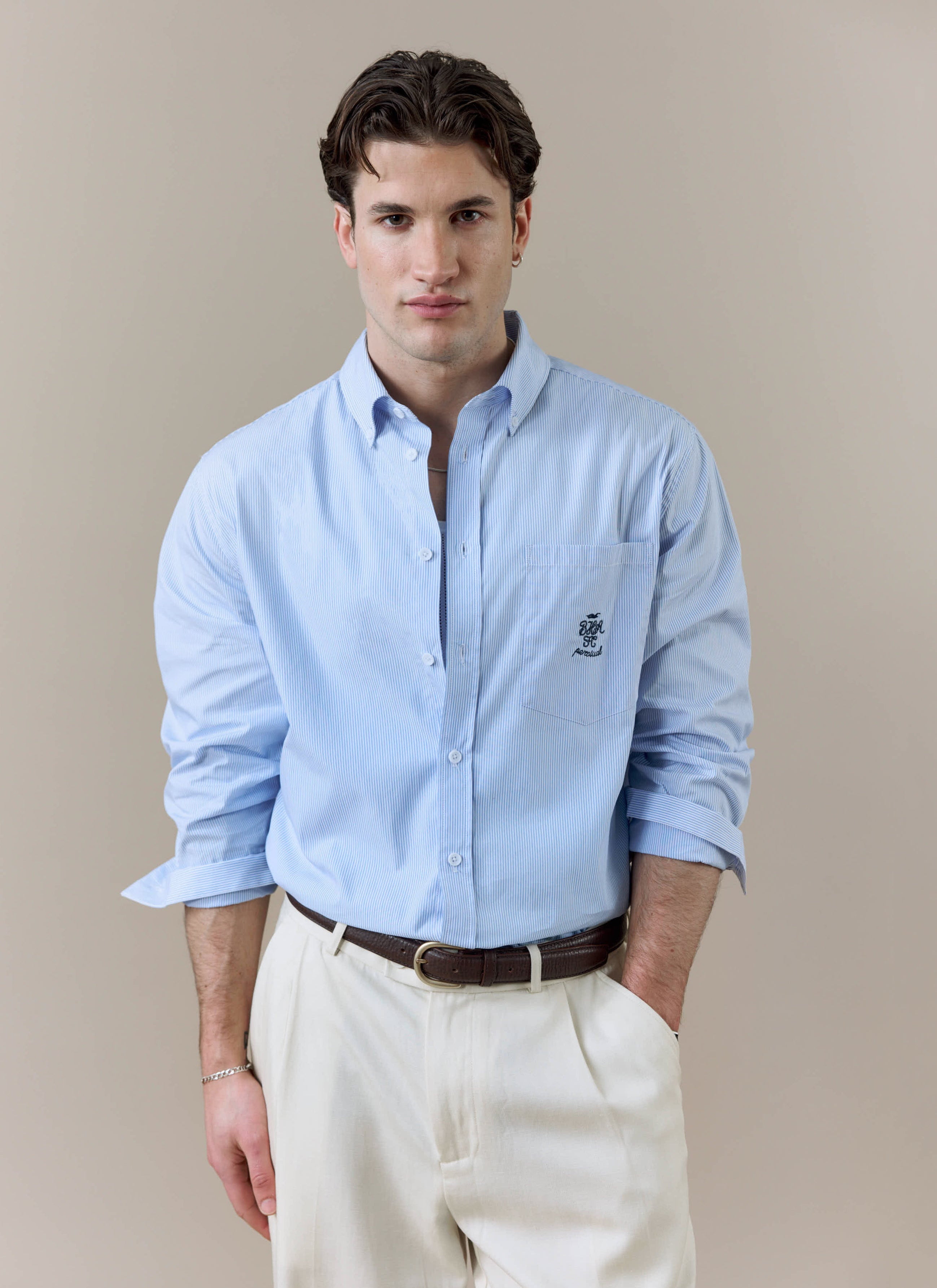 A model wears the Percival x Brighton & Hove Albion F.C. striped Pearce shirt, styled with white trousers.