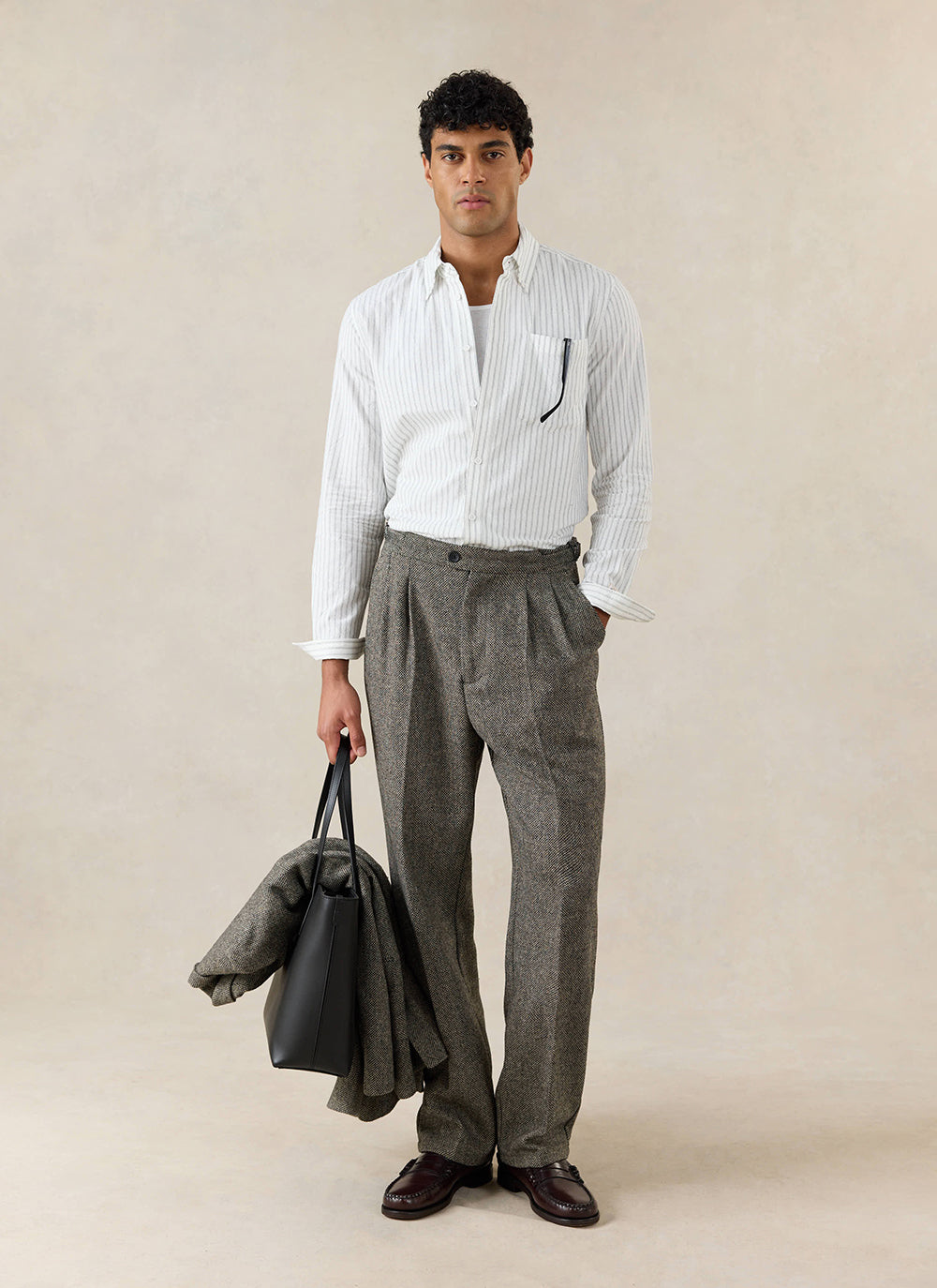 A model wears the Percival Fabian striped shirt, styled with grey textured trousers and a black leather tote bag.