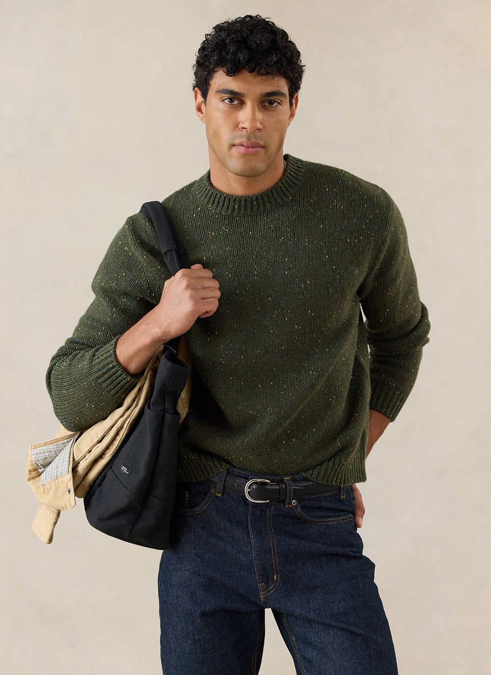 The forest green Percival Rhodes crew neck jumper with colourful speckles, styled with dark jeans and a black bag.
