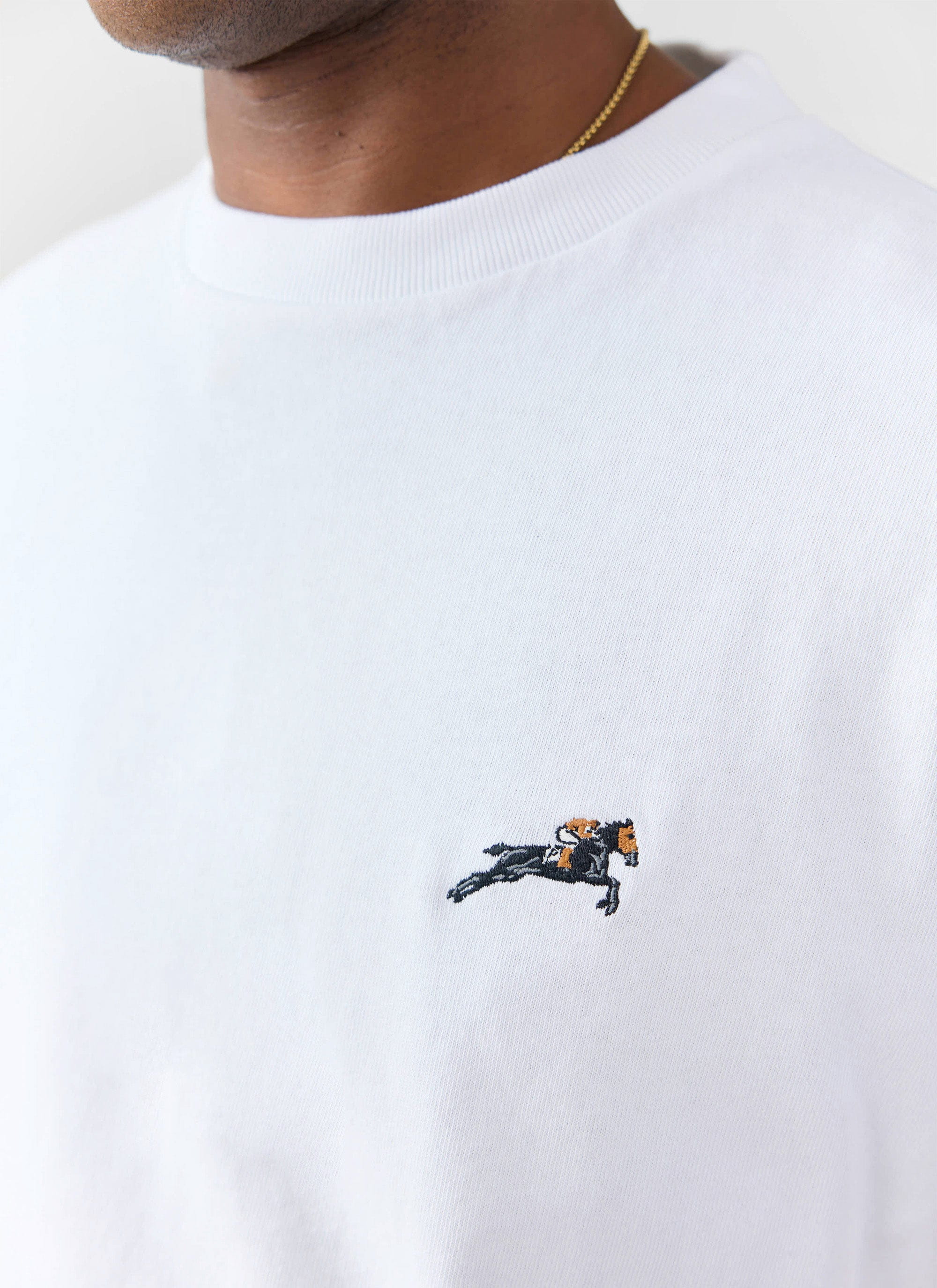 A close-up of the galloping horse embroidery on the chest of the white organic cotton T-shirt from Percival.
