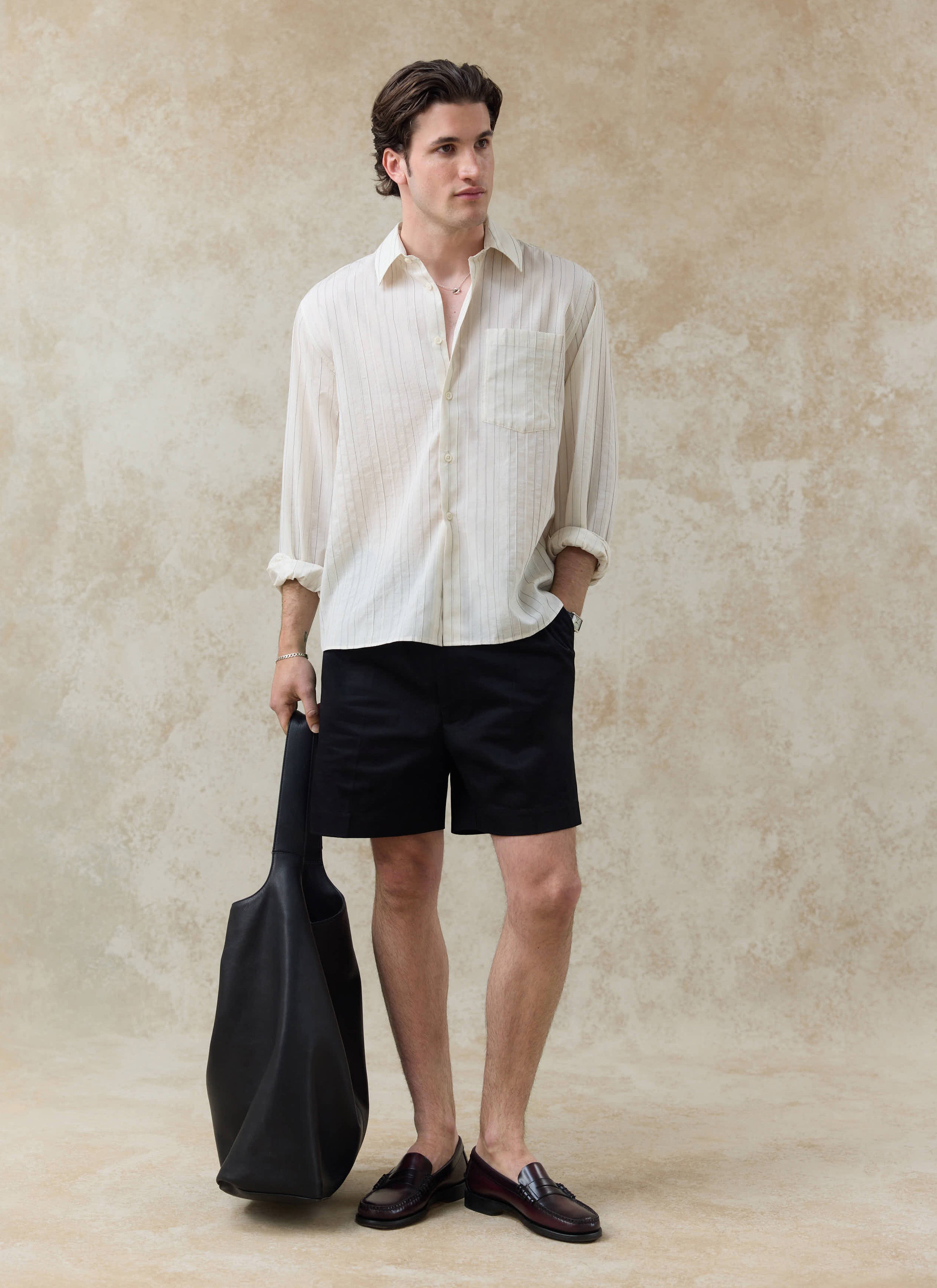 The Percival Lorenzo Pearce Shirt in cream stripe, a lyocell blend button-up styled with black shorts and a leather bag.