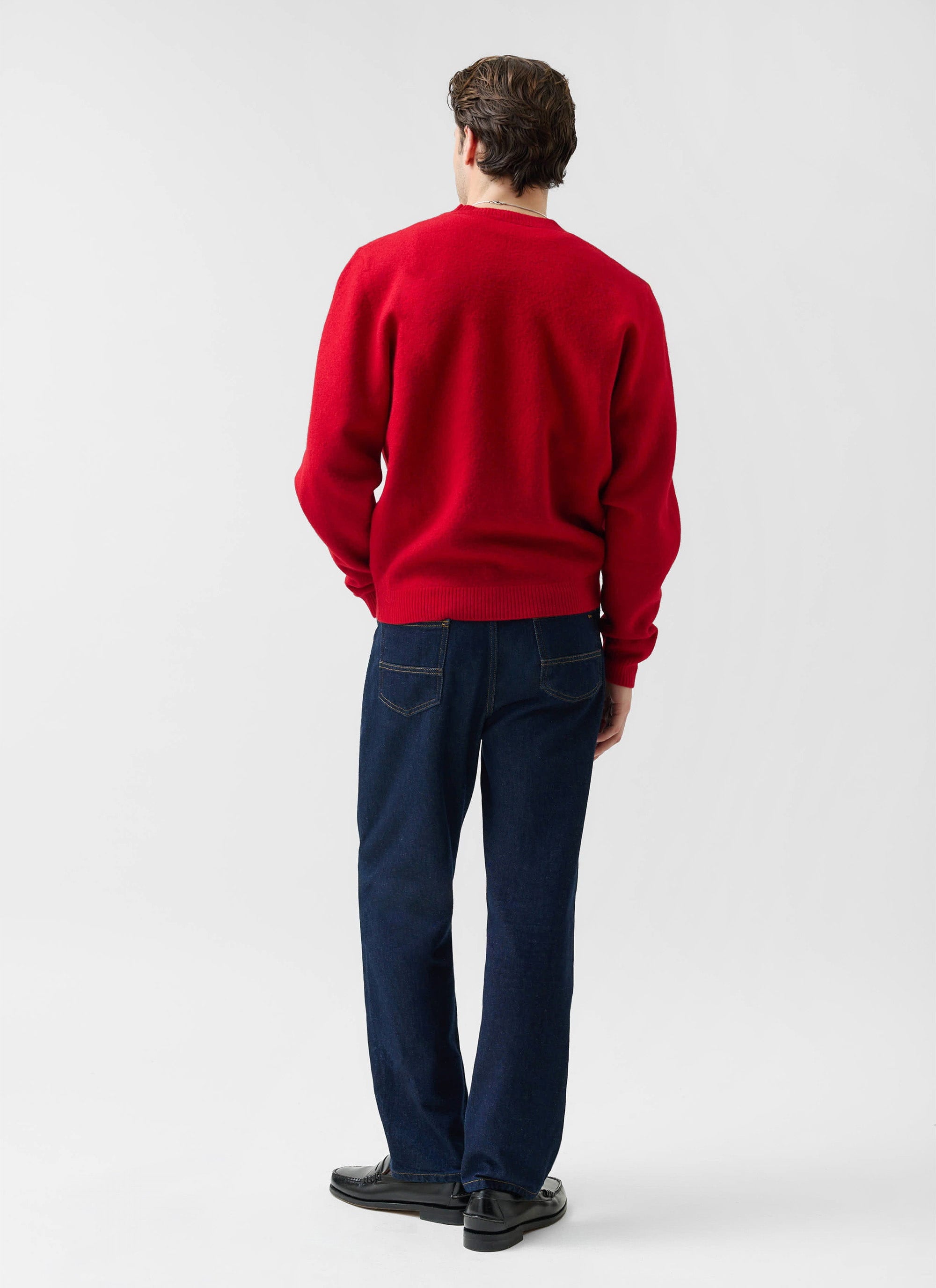Back view of a model wearing the red Felted Regular Jumper in merino wool from Percival, styled with dark blue jeans.