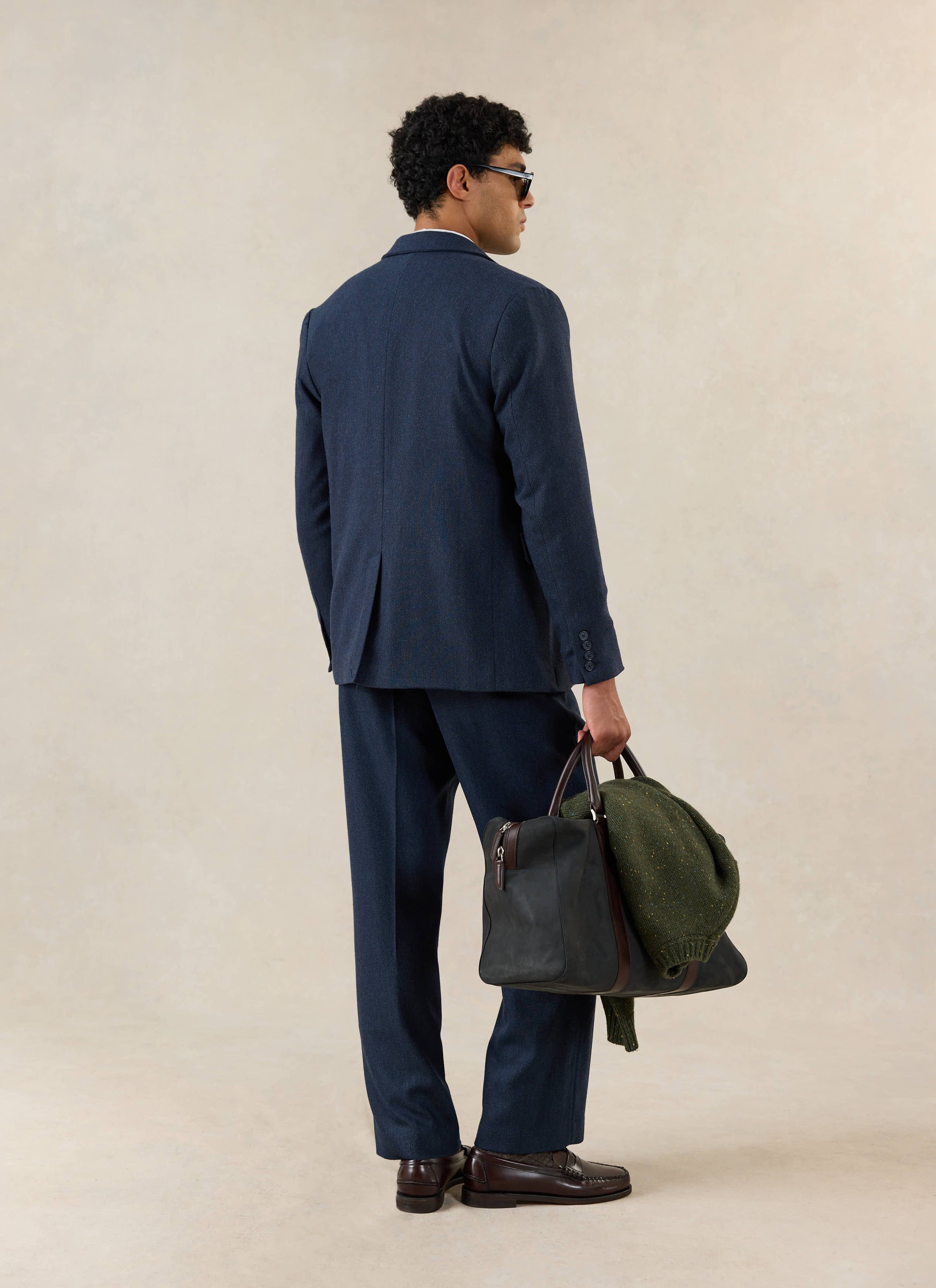 A model wears the Percival Stanley Tailored Blazer in navy herringbone wool, styled with matching trousers and a bag.