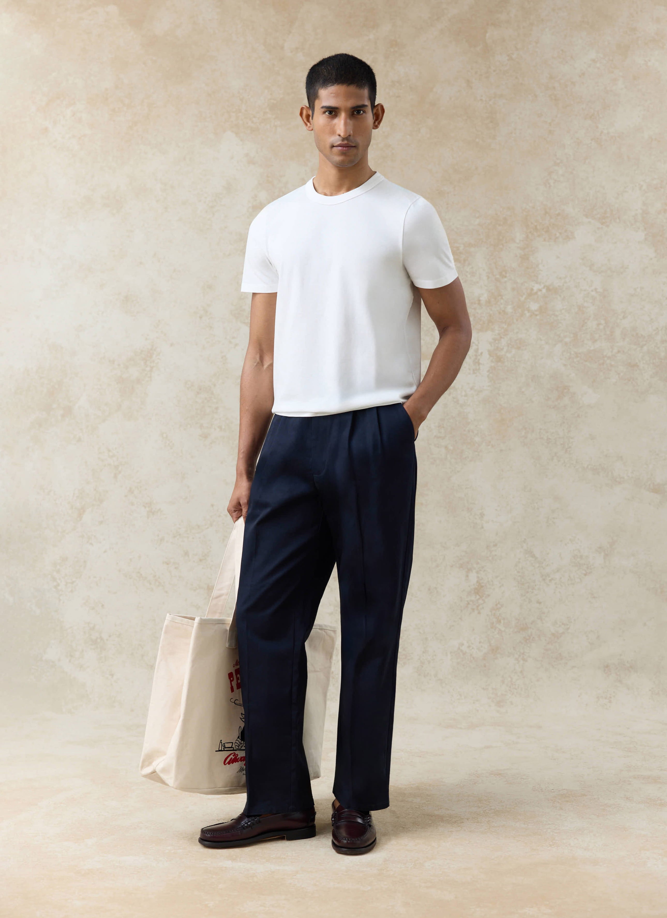 Navy Percival Blake double pleated cotton trousers and an off-white Austin slub t-shirt with a canvas tote bag.
