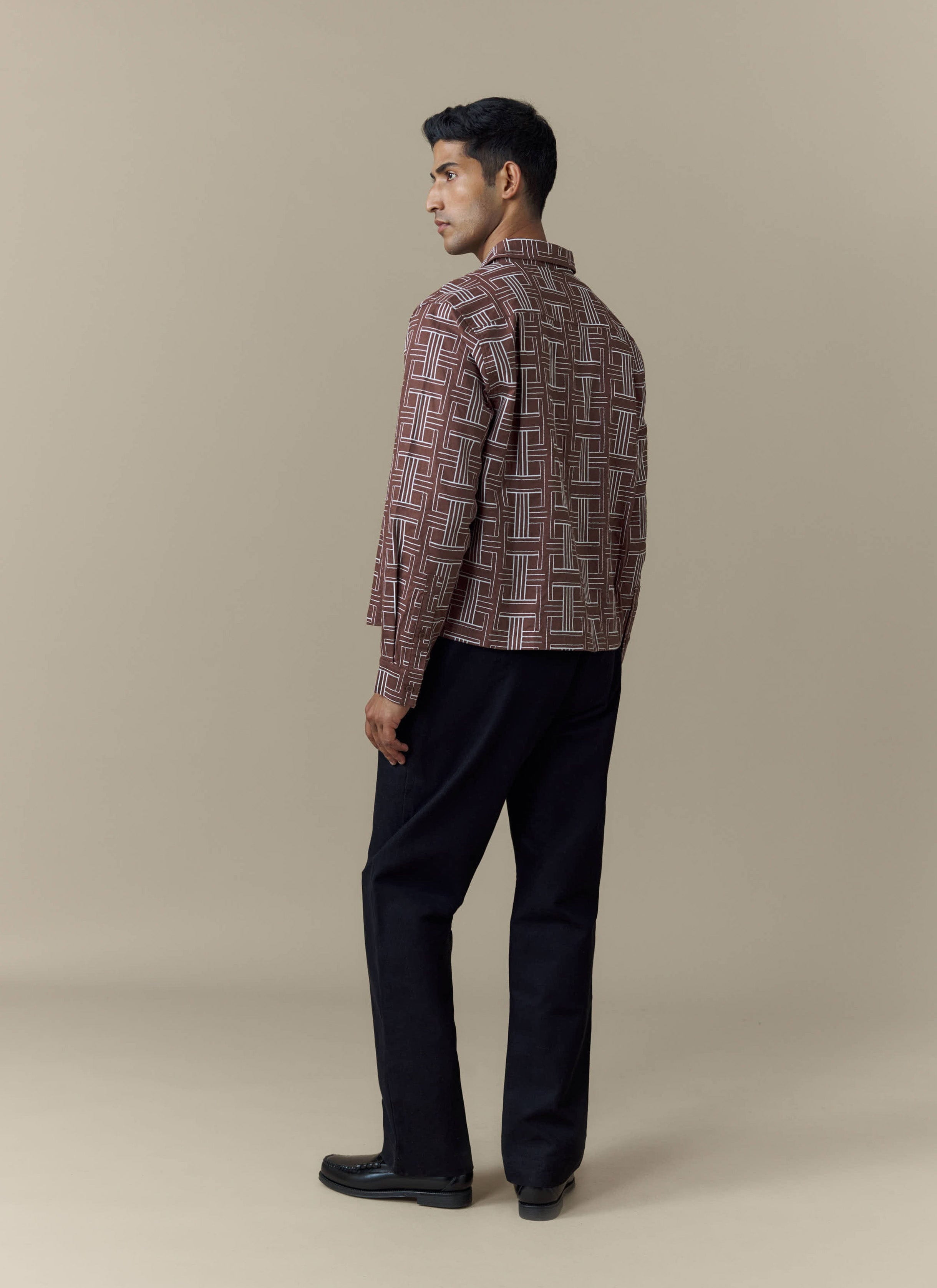 A model seen from a three-quarter back view, wearing the brown patterned Sashiko Boxy Shirt from Percival with dark trousers.