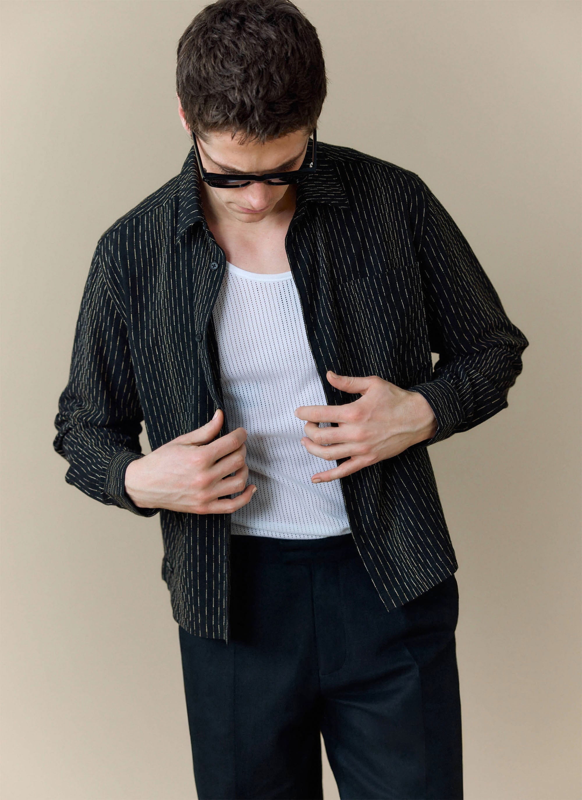 A model wears the black Leland Cuban Boxy Shirt from Percival, styled open over a white vest and black trousers.
