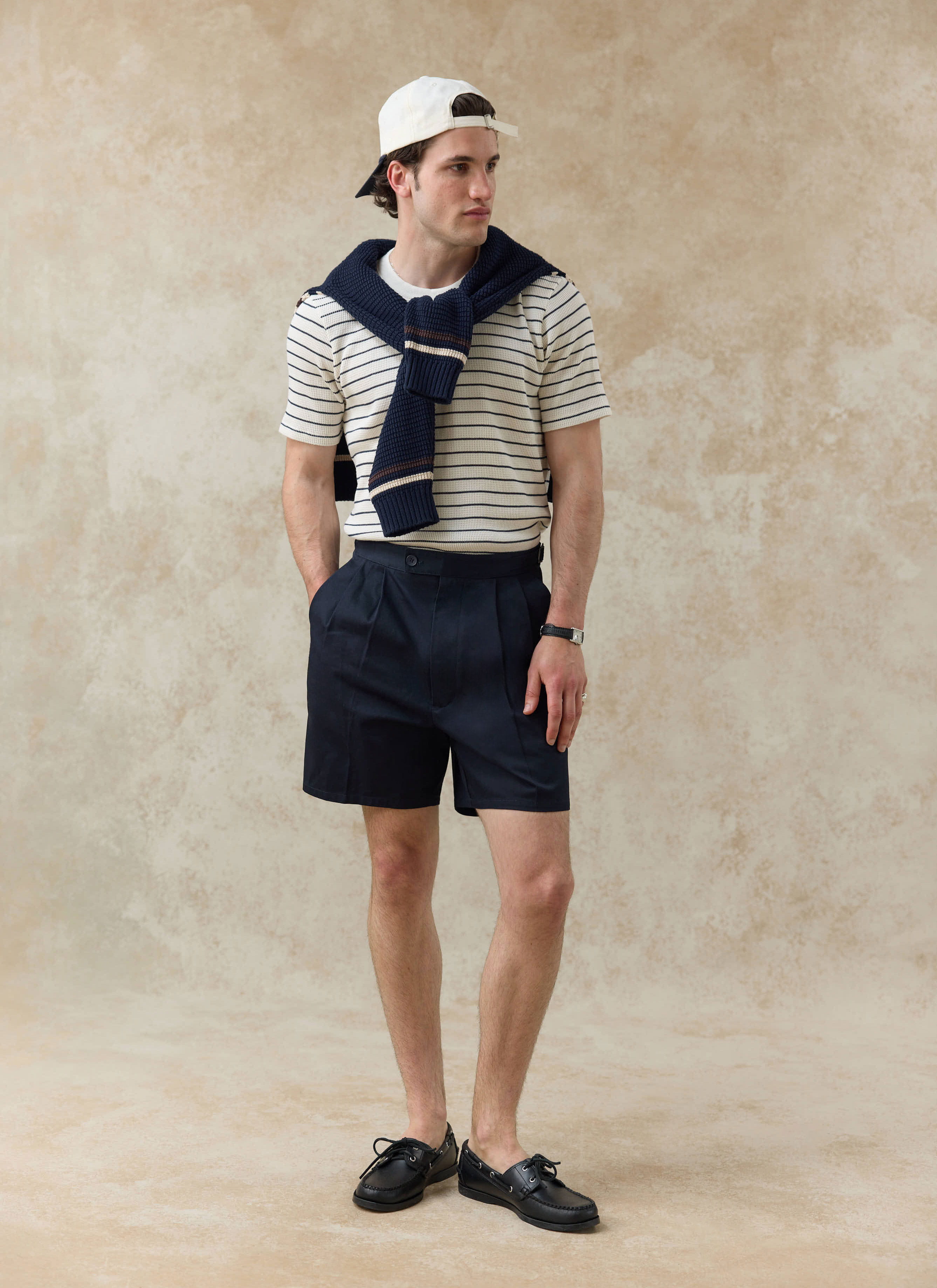 Model wearing Percival navy Blake pleated cotton shorts and a cream striped Ernie waffle T-shirt with a navy knit.