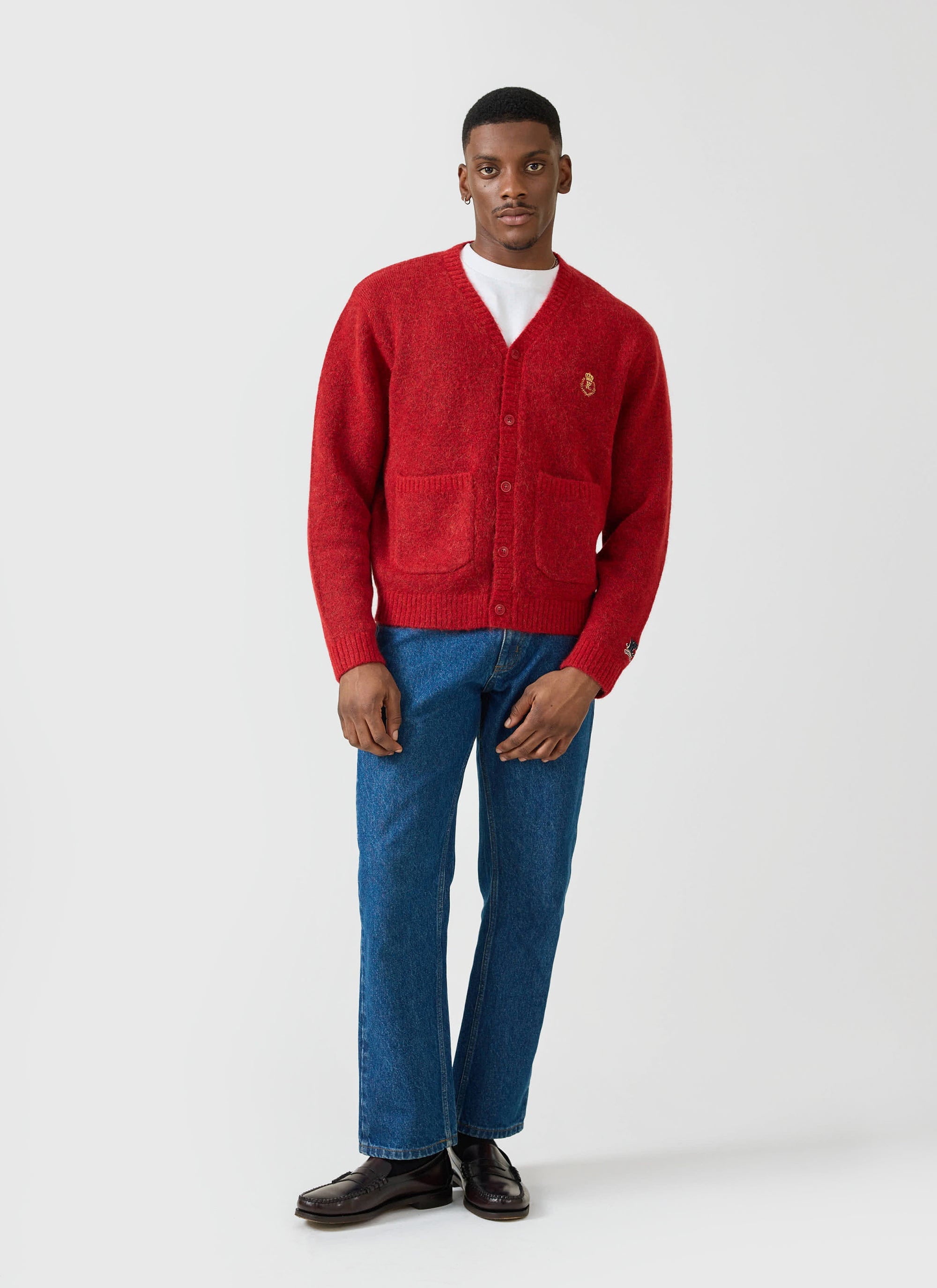 A model wears the red Champion x Percival White Glove knitted cardigan, styled with blue jeans in a studio.
