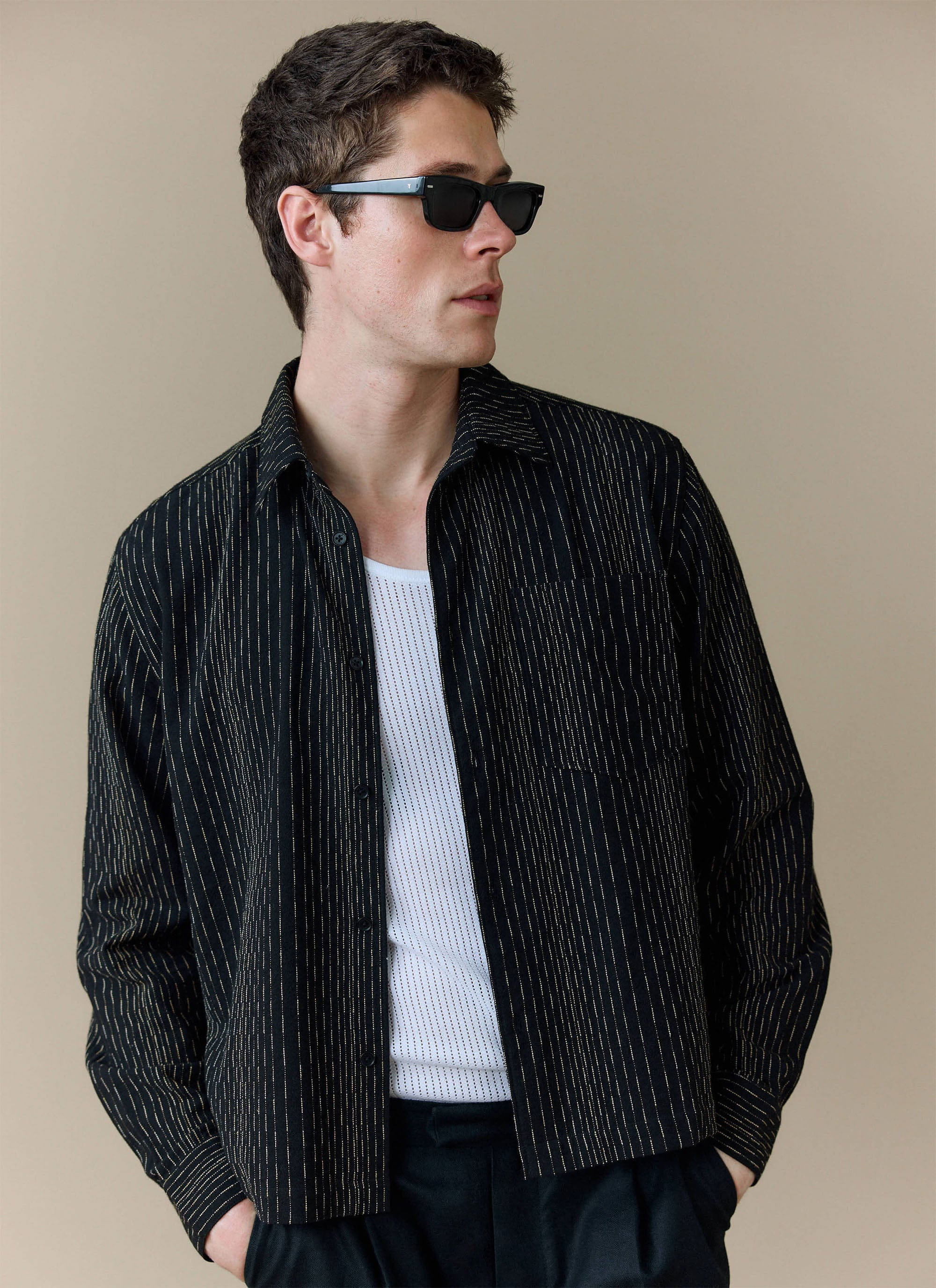 A model wears the black Percival Leland Cuban Shirt with fine vertical stripes, open over a white vest with sunglasses.