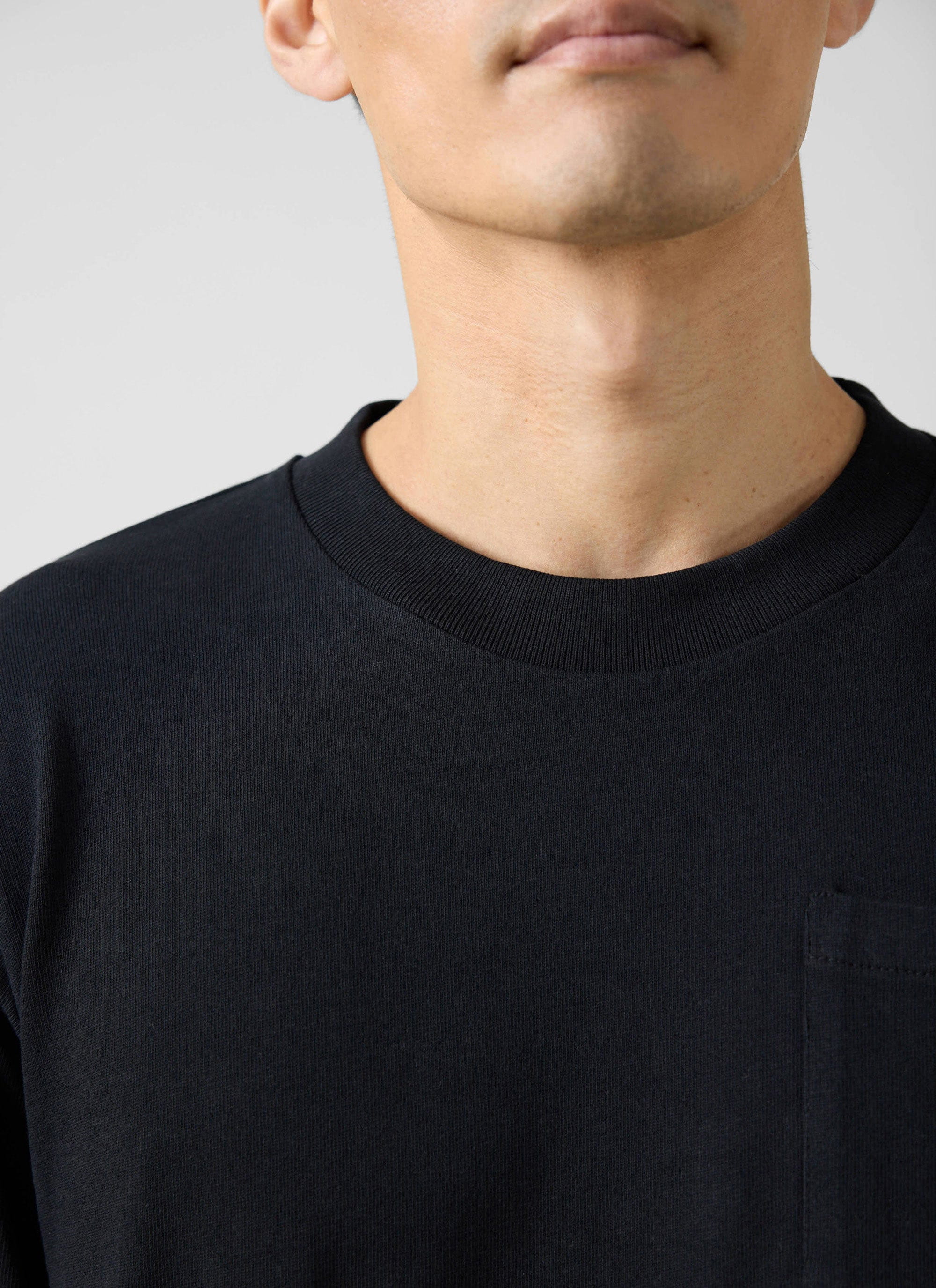 Close-up of the ribbed crew neck and chest pocket on the black organic cotton Long Sleeve Pocket T-Shirt from Percival.