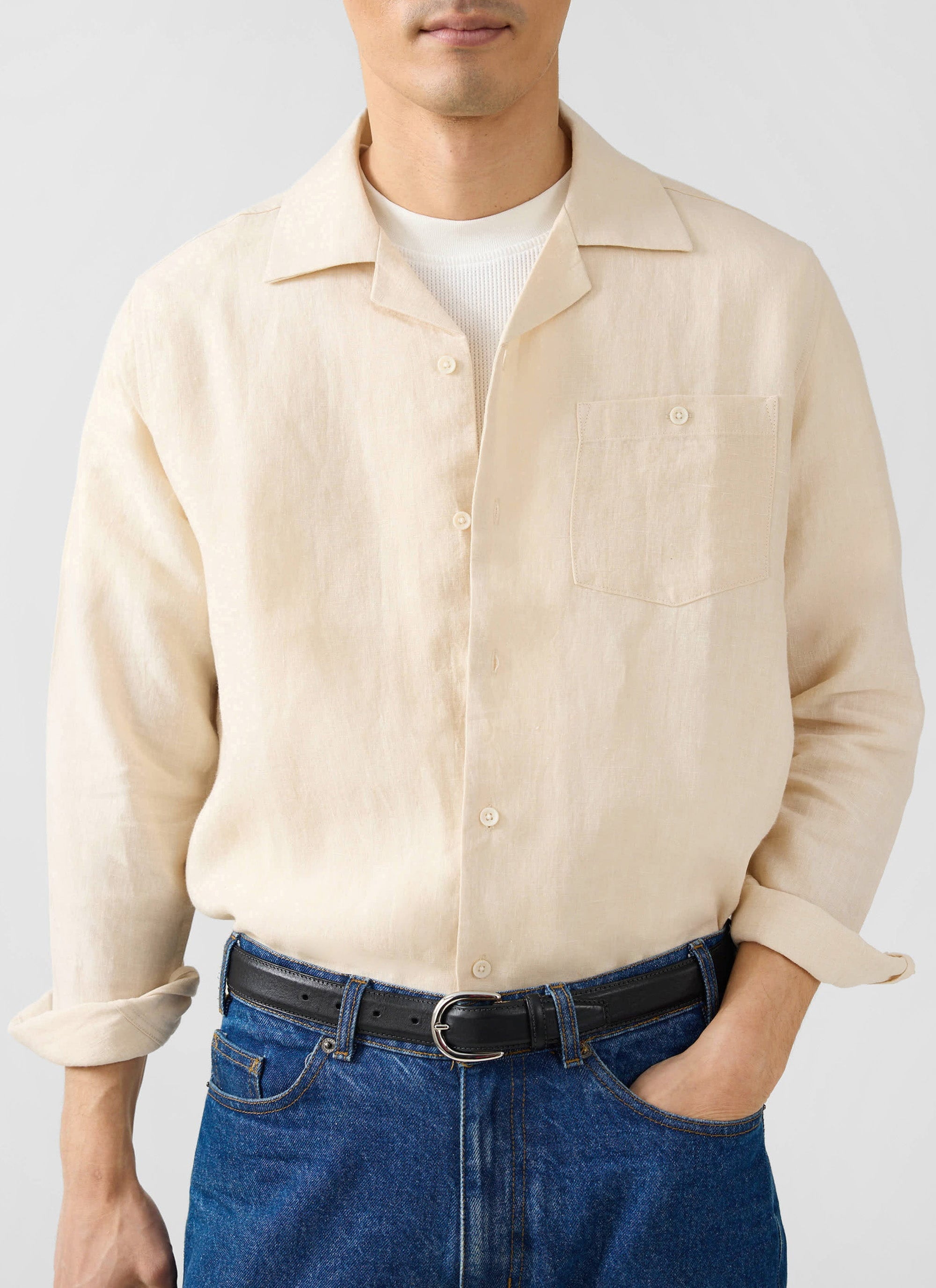 A man wears the Percival Long Sleeve Cuban Linen Shirt in cream, styled open over a t-shirt with blue jeans.