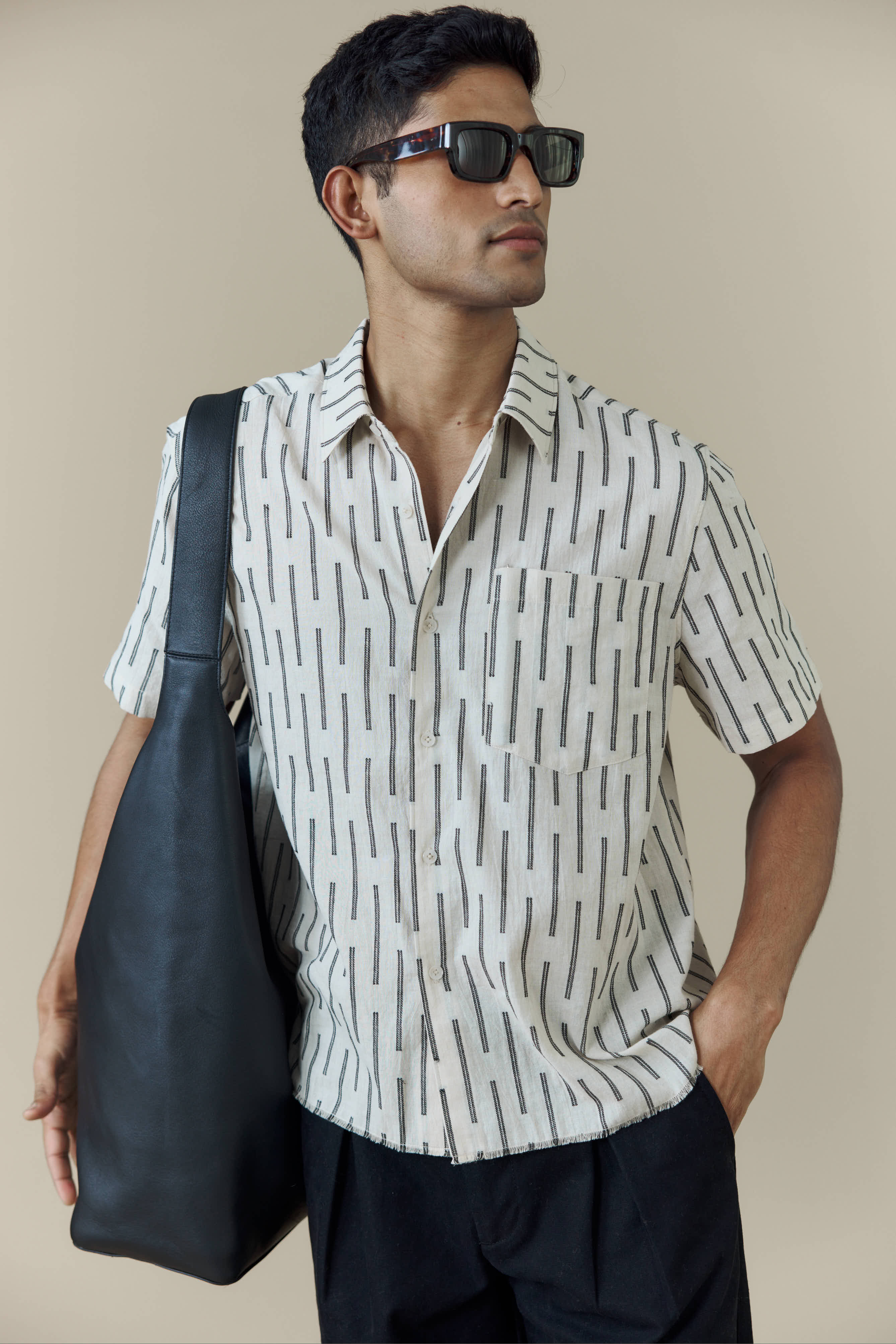 A model wears the Percival Nancy Boxy Shirt in ecru with black stripes, styled with sunglasses and a black shoulder bag.