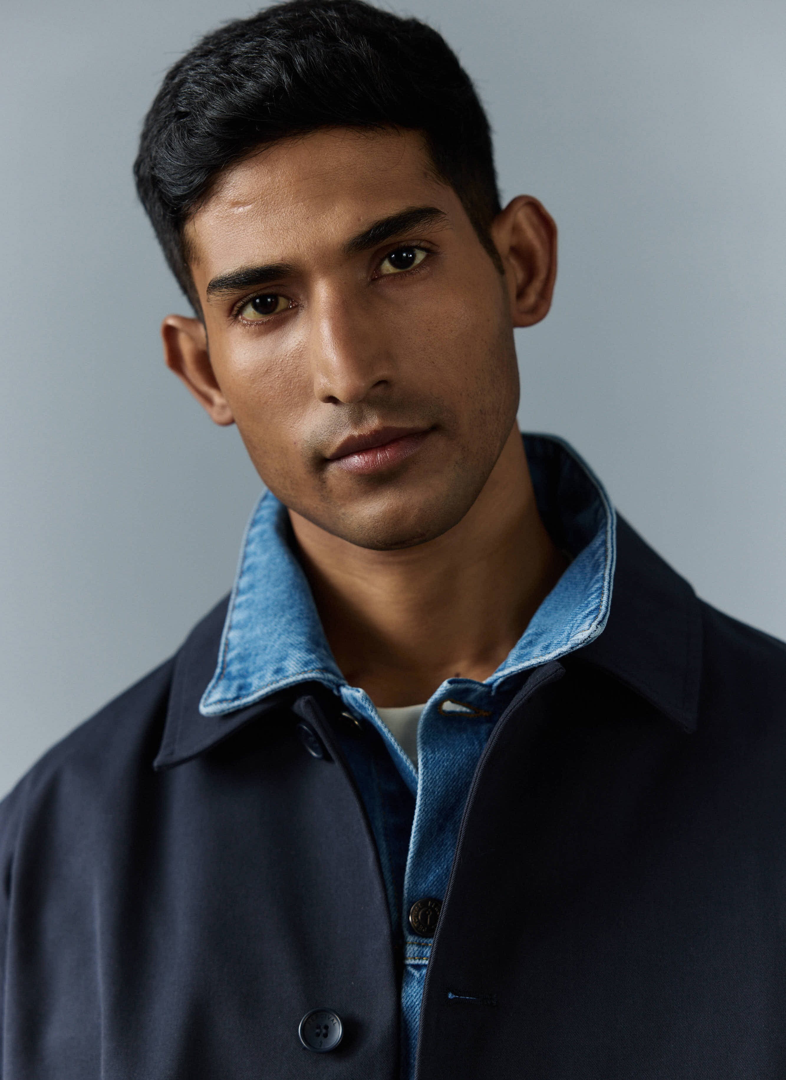 A close-up of a model wearing the Percival navy Sherlock Short Trench Coat layered over a blue denim jacket.