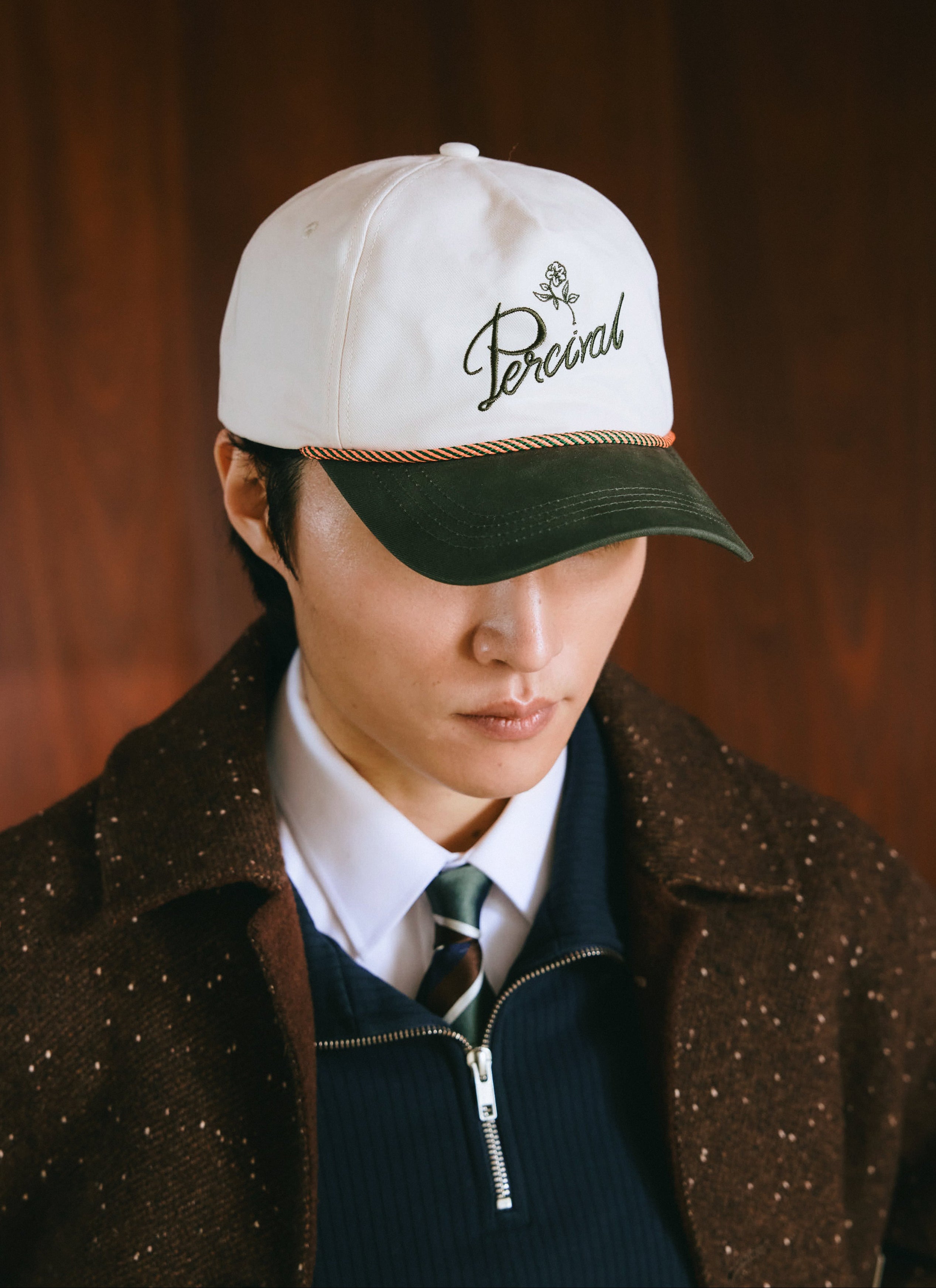 A model wearing a Percival soft trucker cap in white with green branding and visor, styled with a tie and jacket.