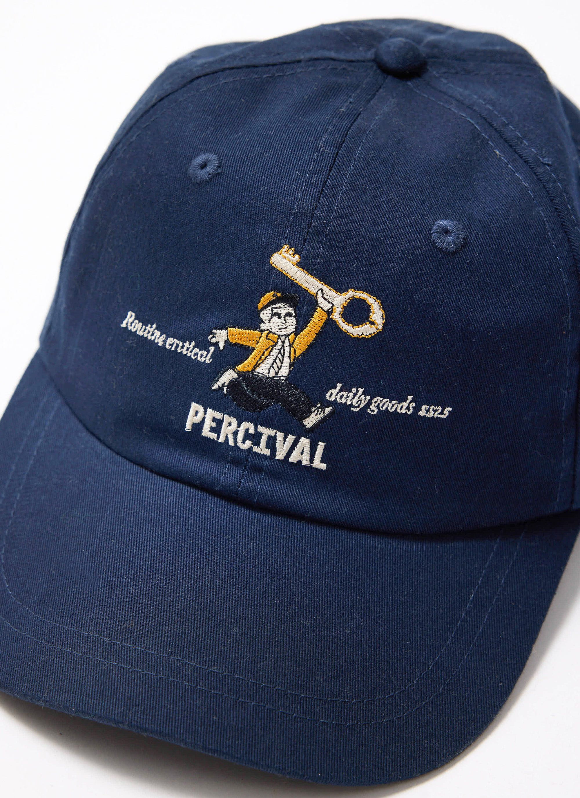 A close-up of the navy cotton World Key Cap by Percival, detailing the 'man with a key' embroidery on the front.