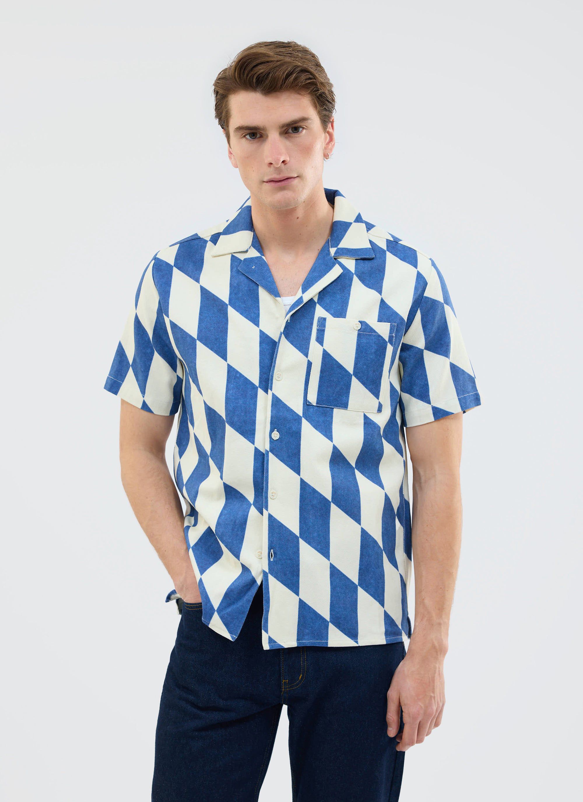 A male model wears the Percival Market Diamond Cuban Shirt, a short sleeve shirt in an ecru and navy diamond print.