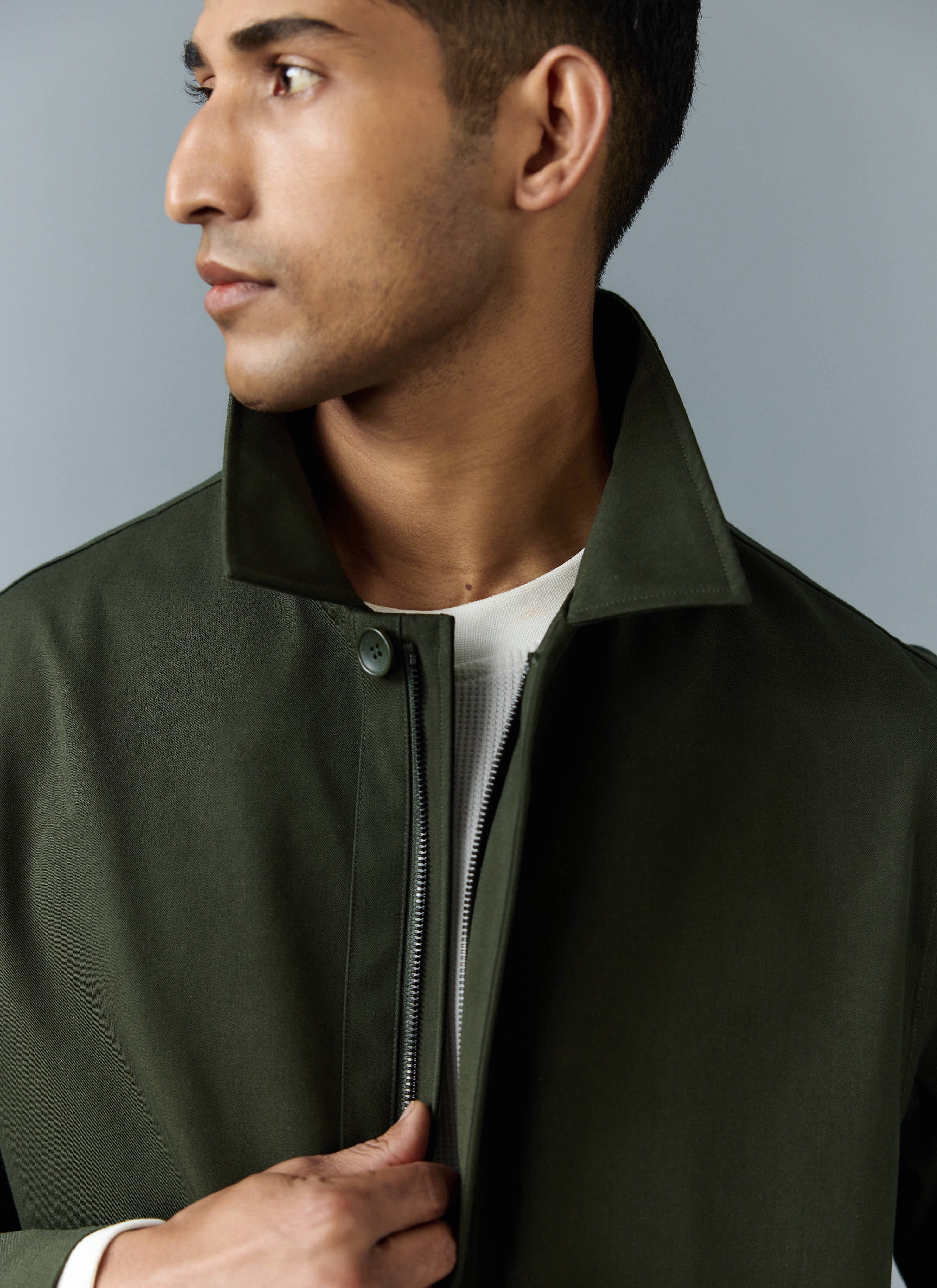 A close-up shot of a model wearing the Percival Greyson Long Trench Coat in forest green, showing the collar and zip detail.