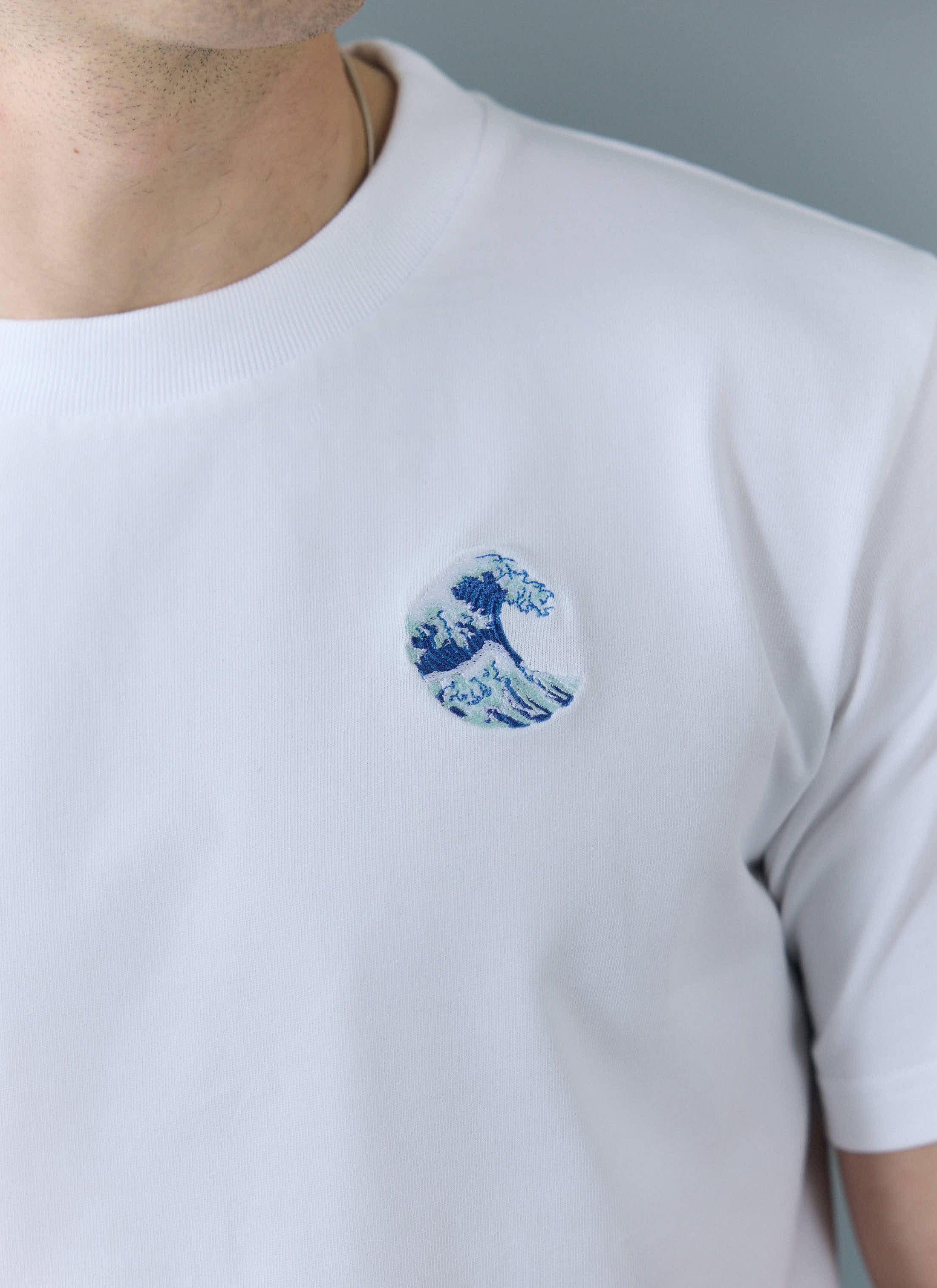 Close up of a model wearing the Percival Wave T-shirt in white, showing the embroidered wave detail on the chest.