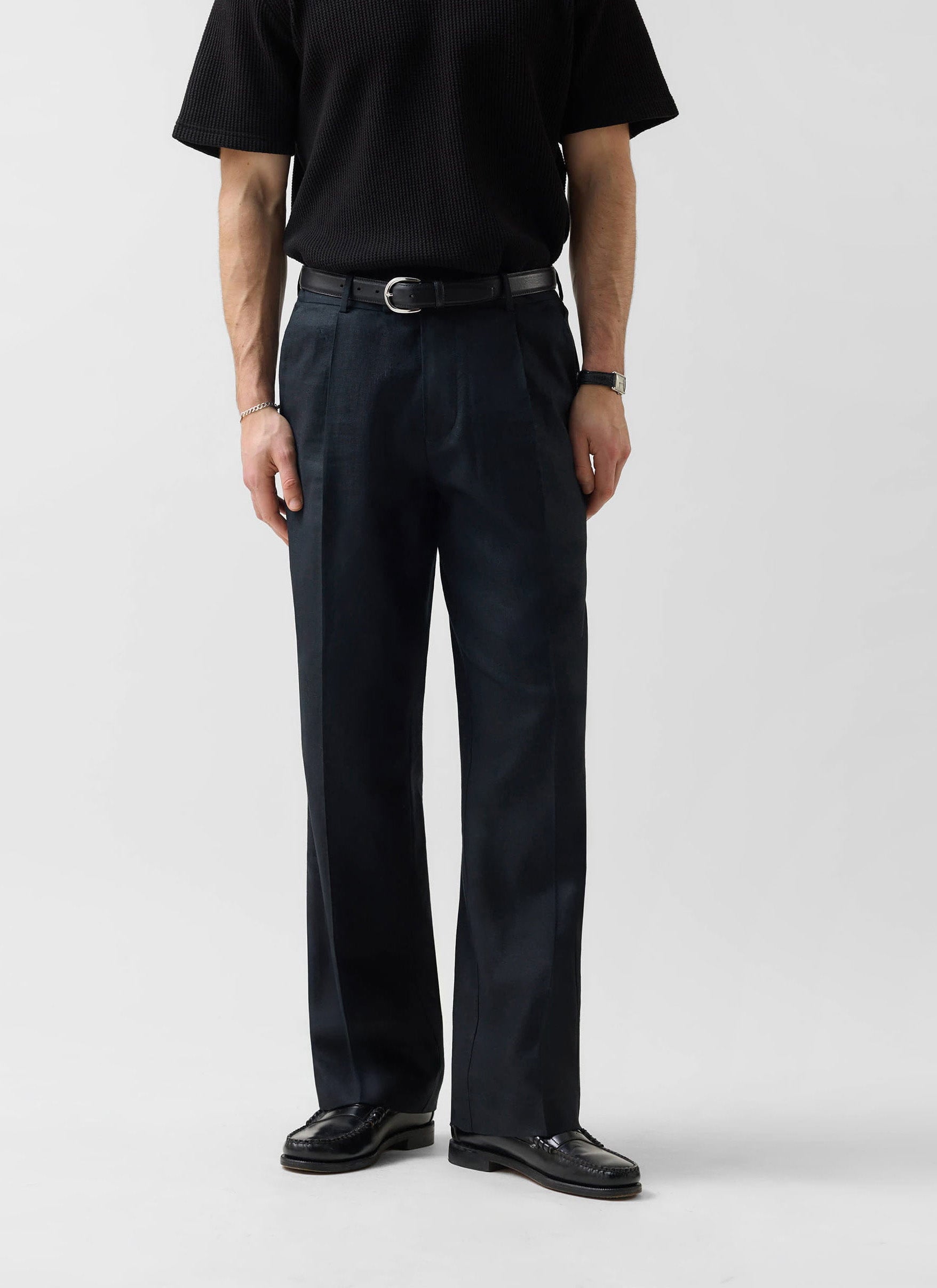 A man models the Percival Wide Leg Trousers in black linen, paired with a black ribbed t-shirt against a white background.