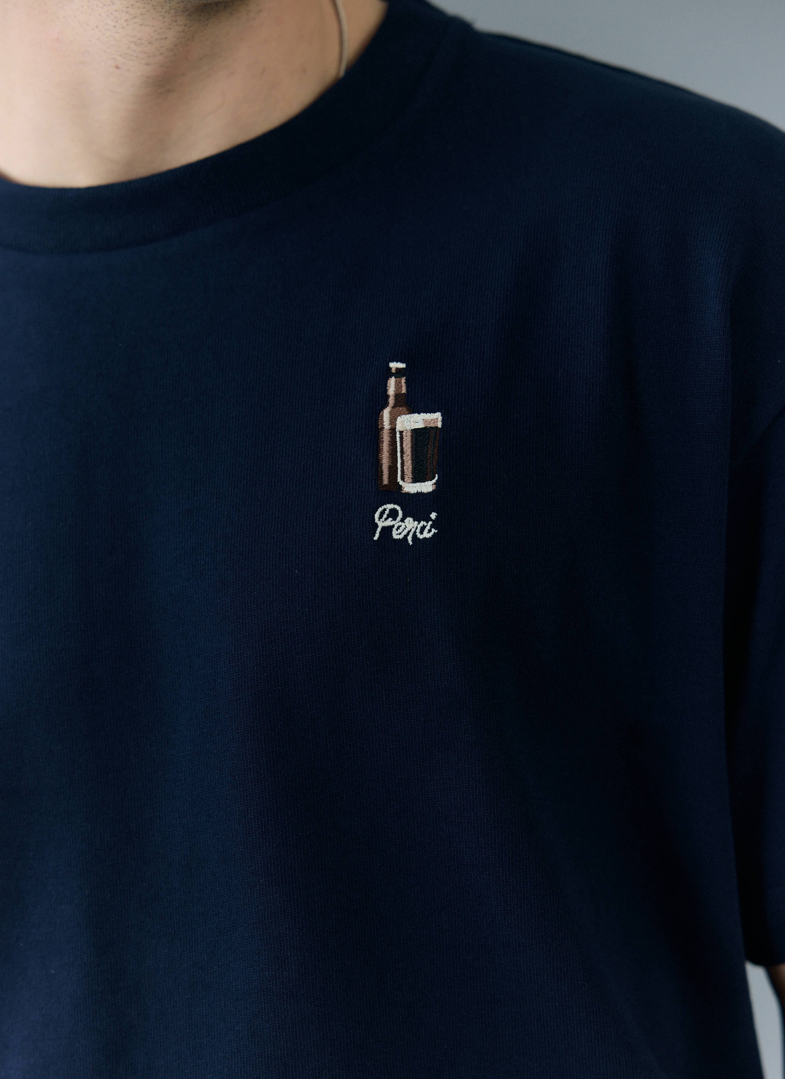 Close-up shot of the Percival Stout Oversized T-Shirt in navy, highlighting the intricate stout and bottle embroidery.