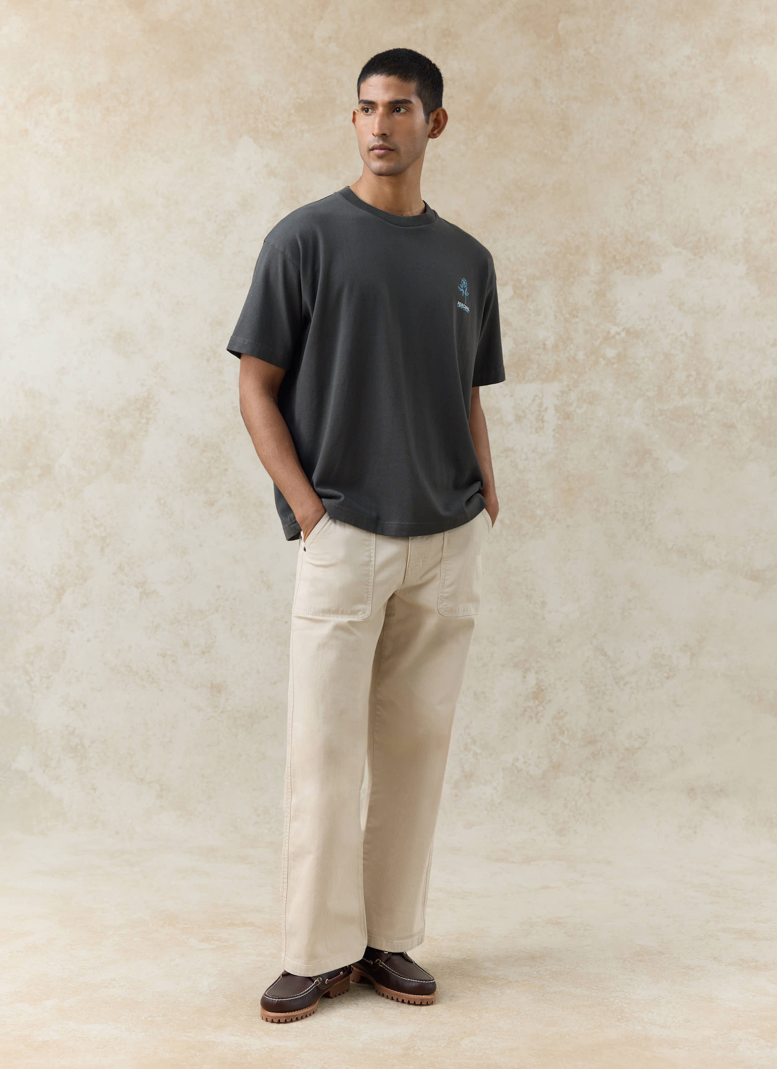 Charcoal grey Percival Otto Oversized T-shirt in organic cotton with a blue graphic, worn by a model with cream trousers.
