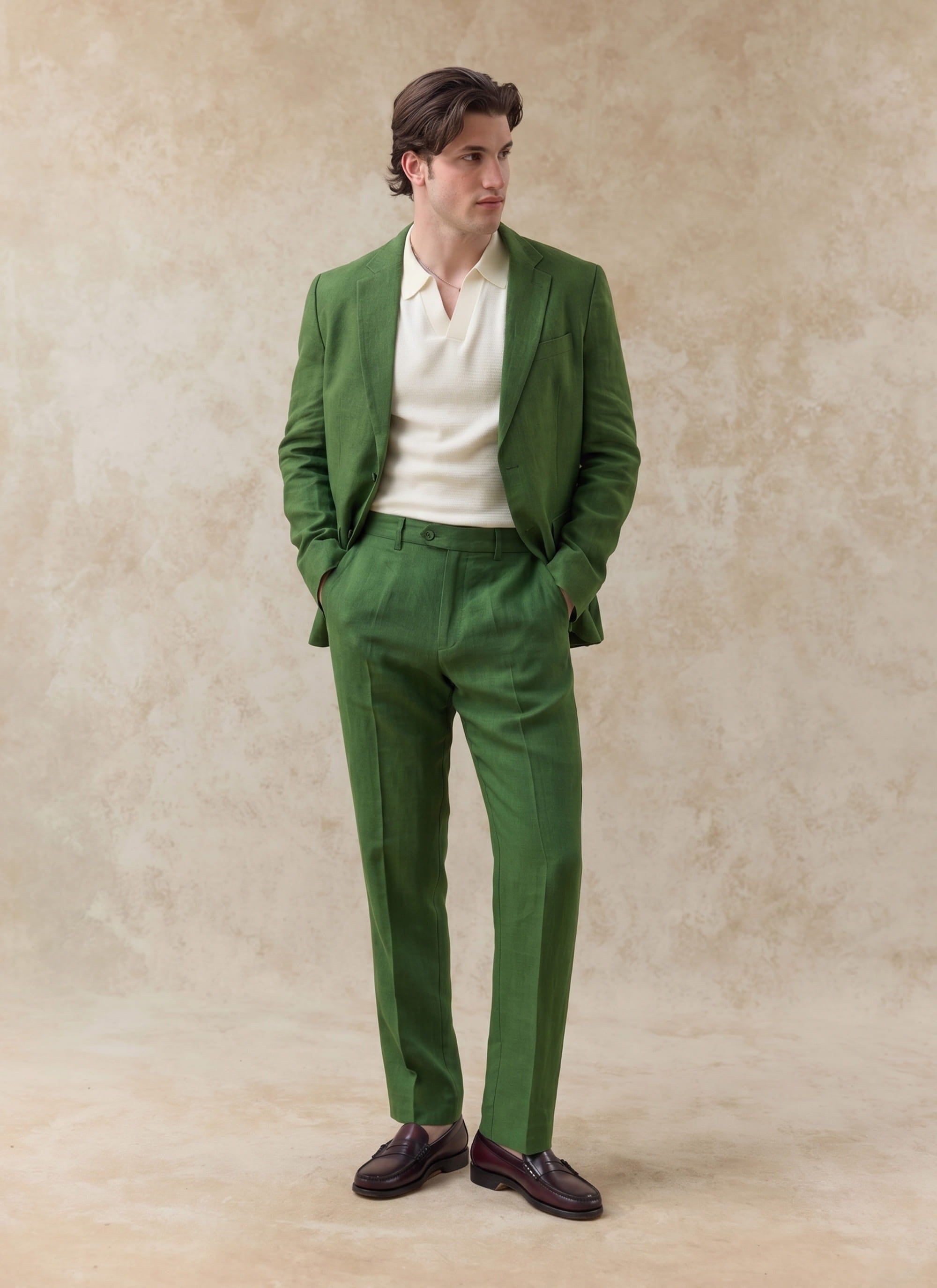 Model wearing forest green Percival tailored linen trousers as part of a matching suit with a cream knit polo.