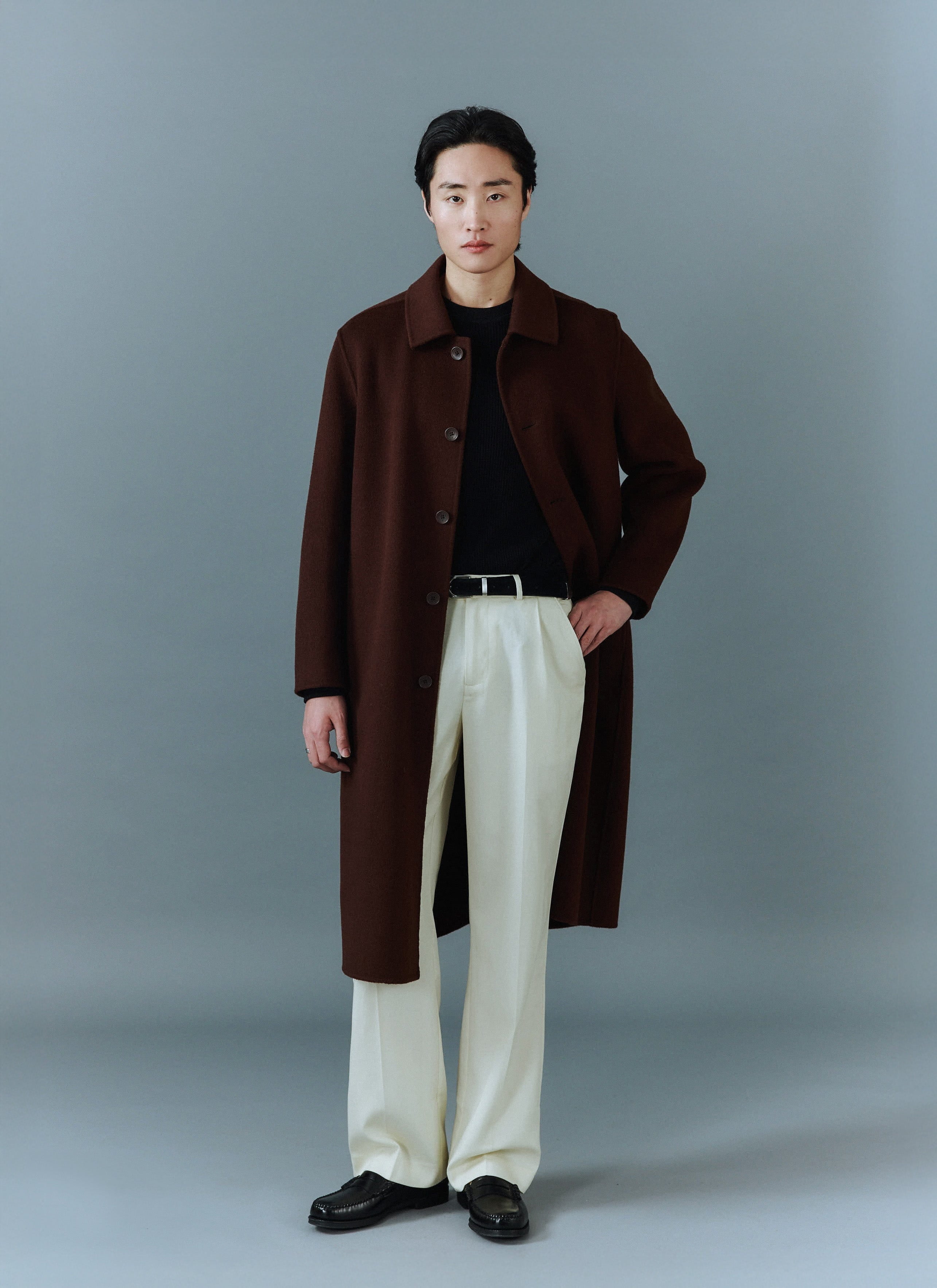 A man models the Percival Minnesota Overcoat in espresso wool, styled with cream trousers and a black knit jumper.