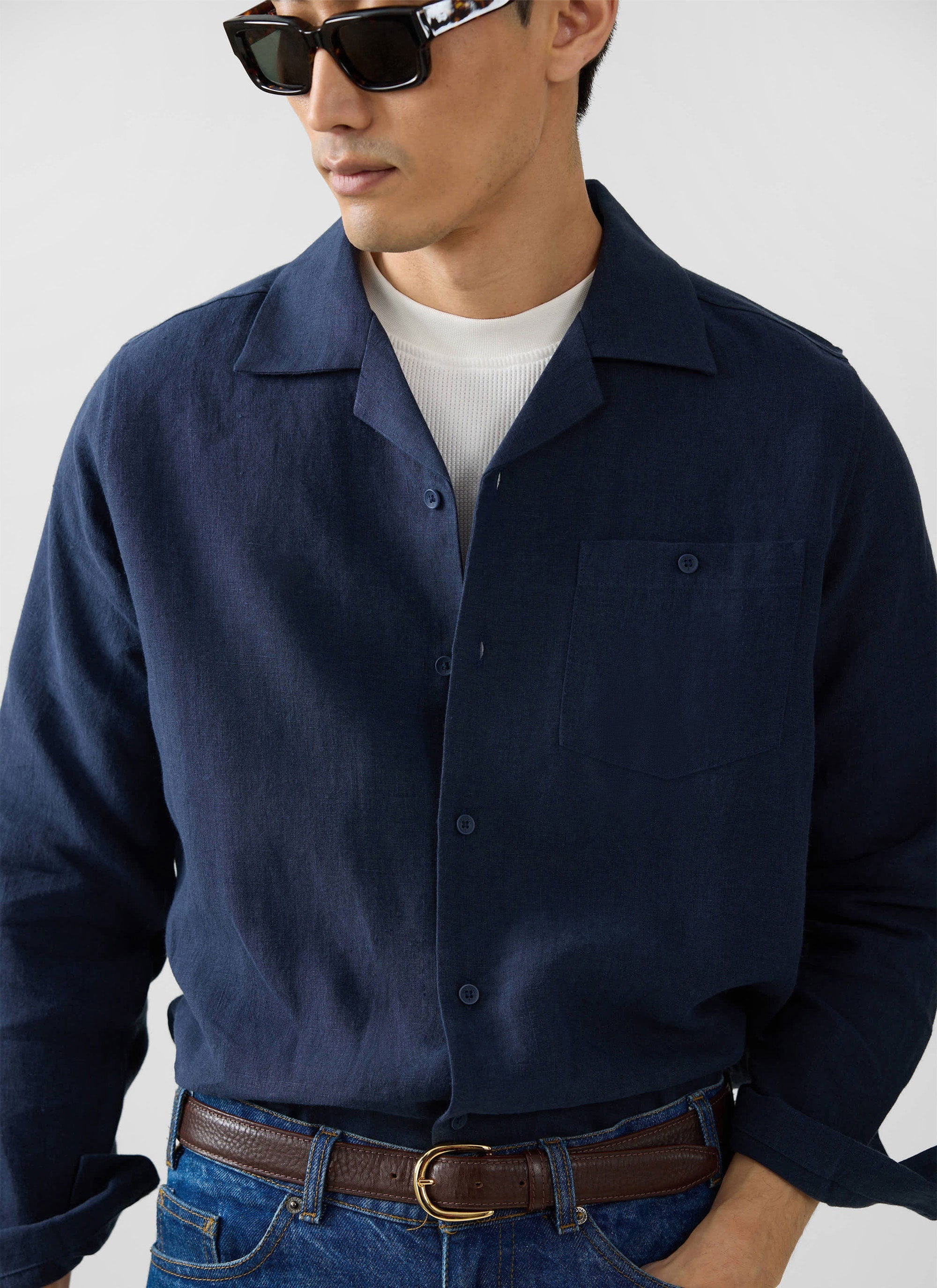 A model wears the Percival Long Sleeve Cuban Linen Shirt in navy with a white t-shirt, jeans, and sunglasses.