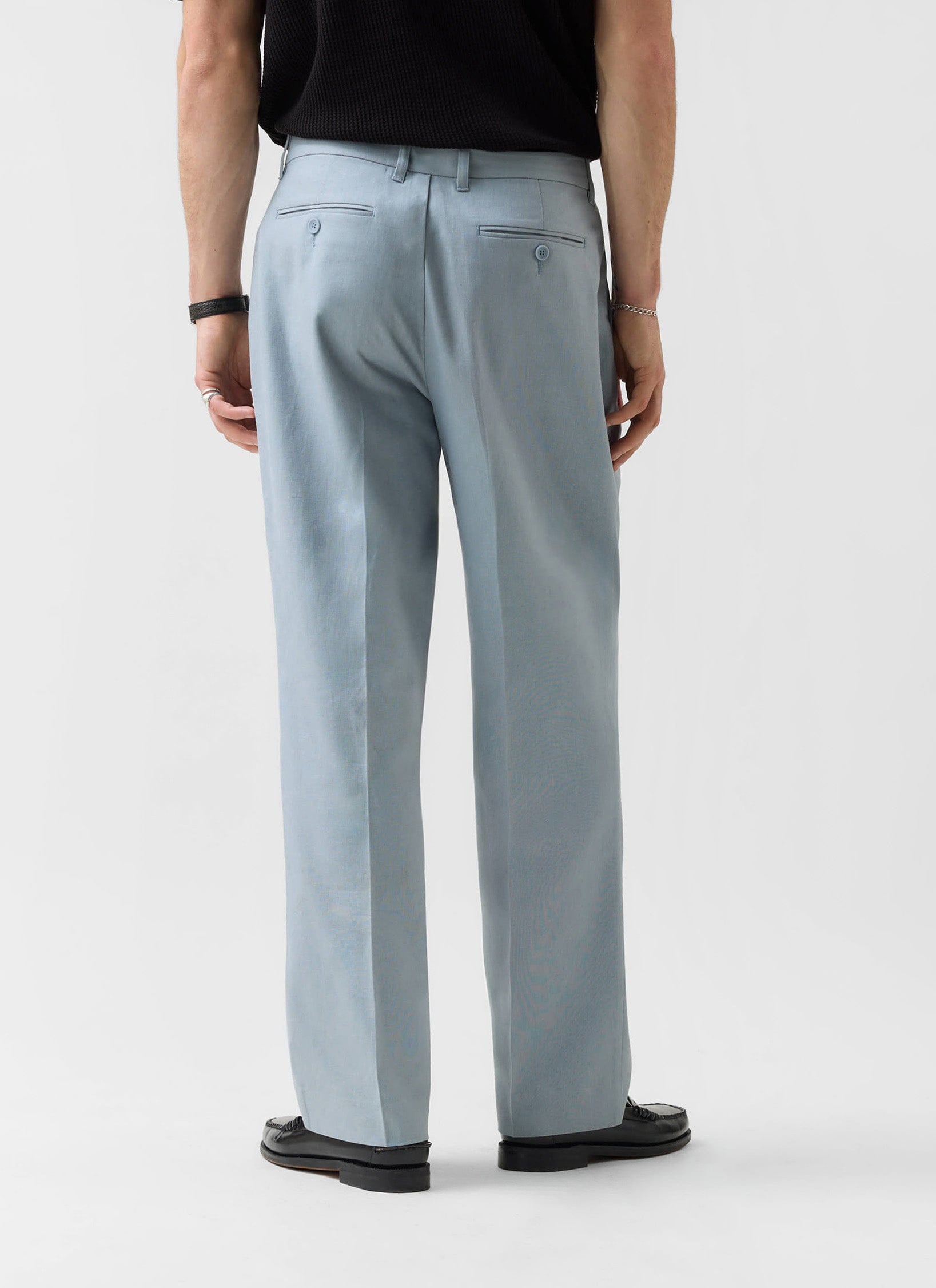 A back view of a man wearing Percival's light blue pleated linen tailored trousers.