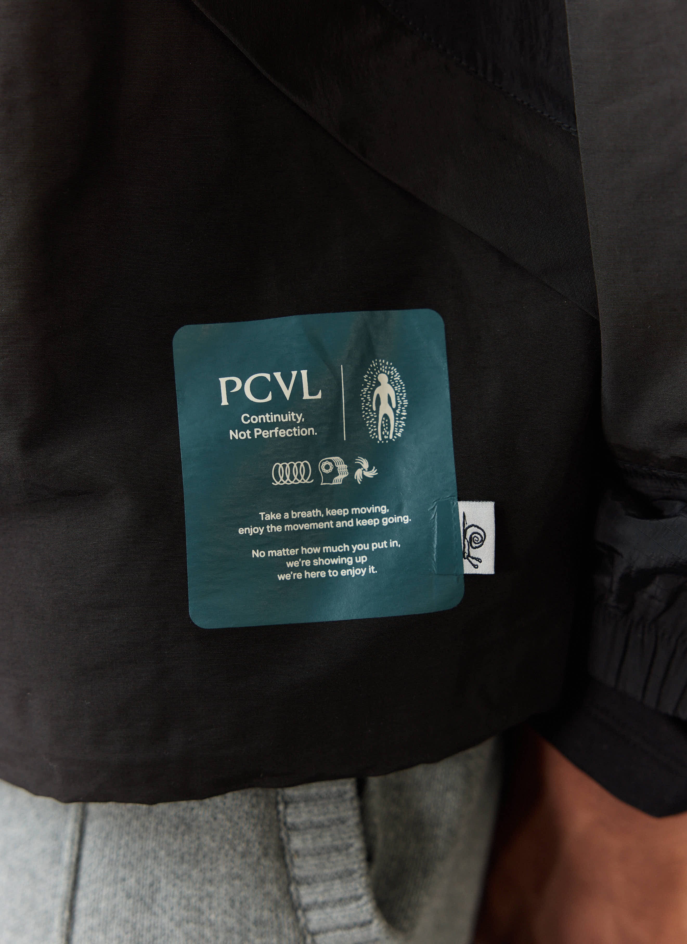 Detail shot of the internal 'Continuity, Not Perfection' patch on the black PCVL jacket by Percival.