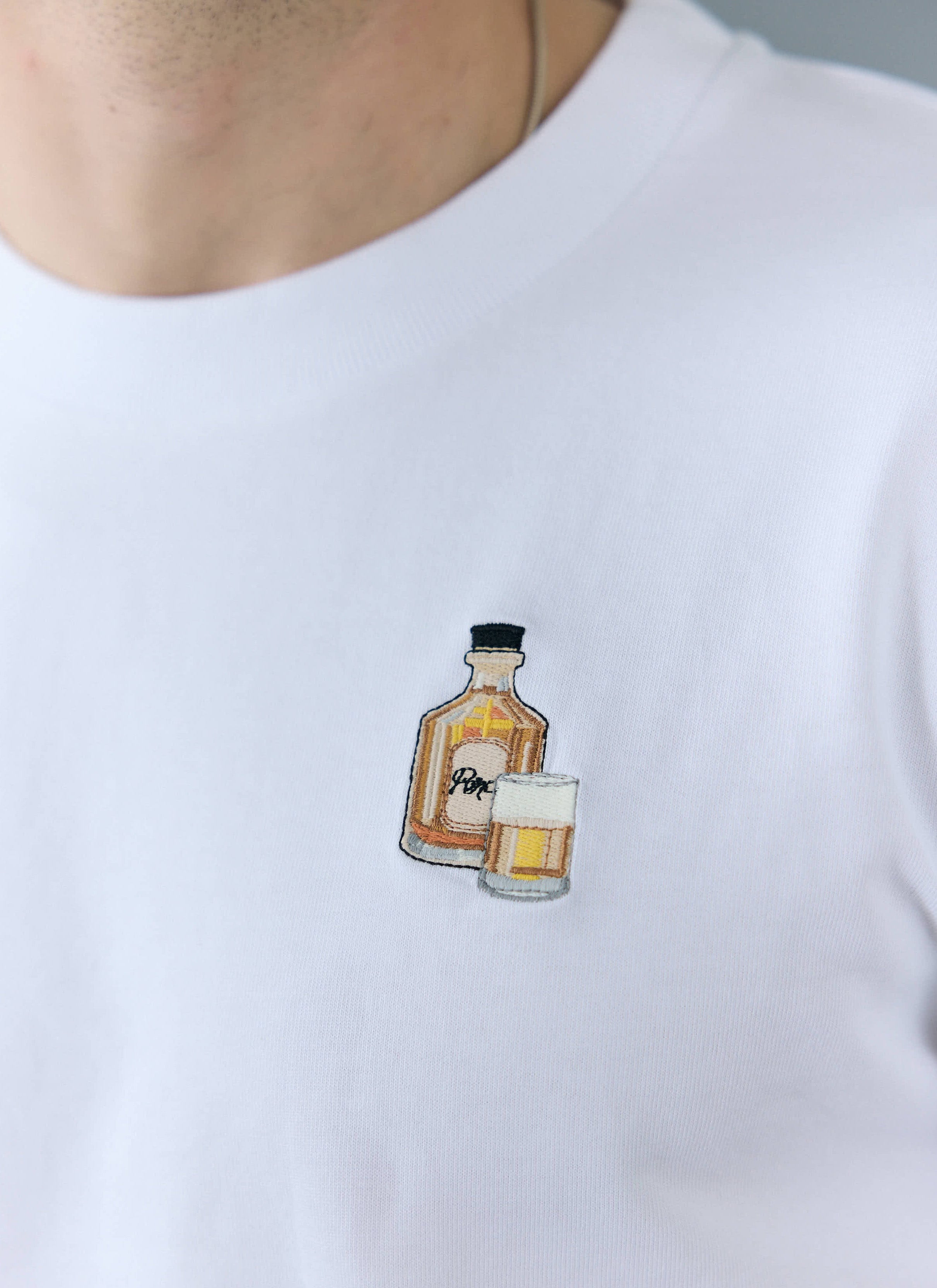 A close-up of the Old Fashioned cocktail embroidery on the chest of the white organic cotton T-shirt from Percival.