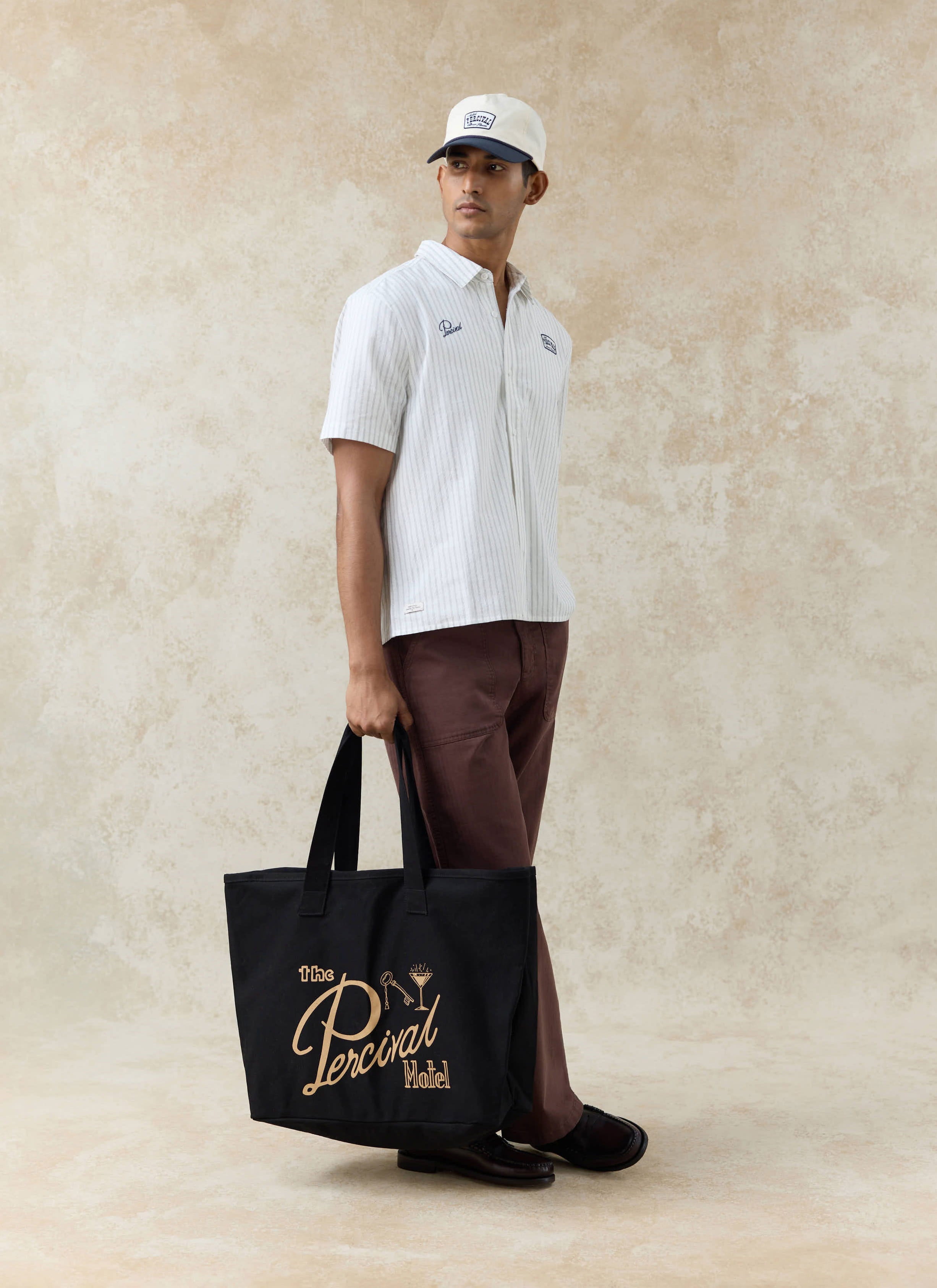 Percival Lucia cream stripe cotton shirt and Donovan trucker cap styled with a large black motel-inspired tote bag.