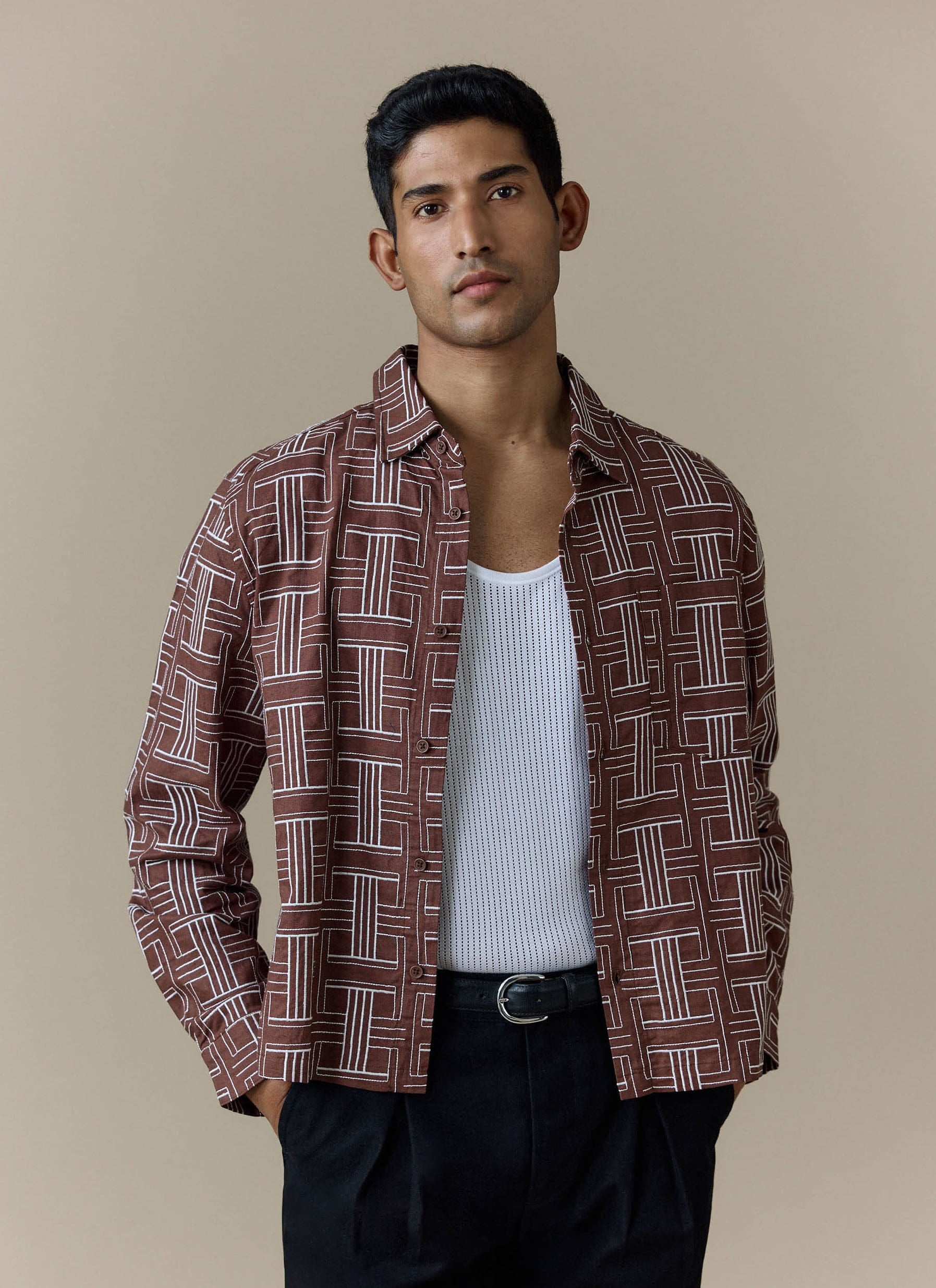 A model wears the brown Percival Sashiko Boxy Shirt open over a white vest and black trousers.